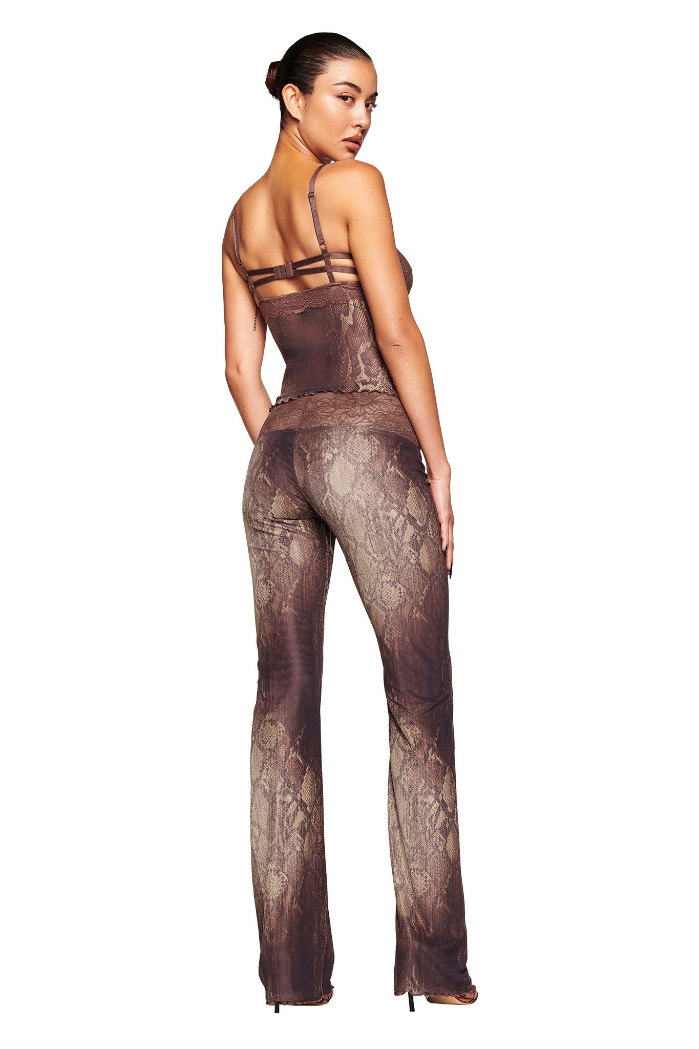 Woman with hair in a bun wears the I.AM.GIA SILO TOP - SNAKE with matching pants, standing with her back to the camera and looking over her shoulder.