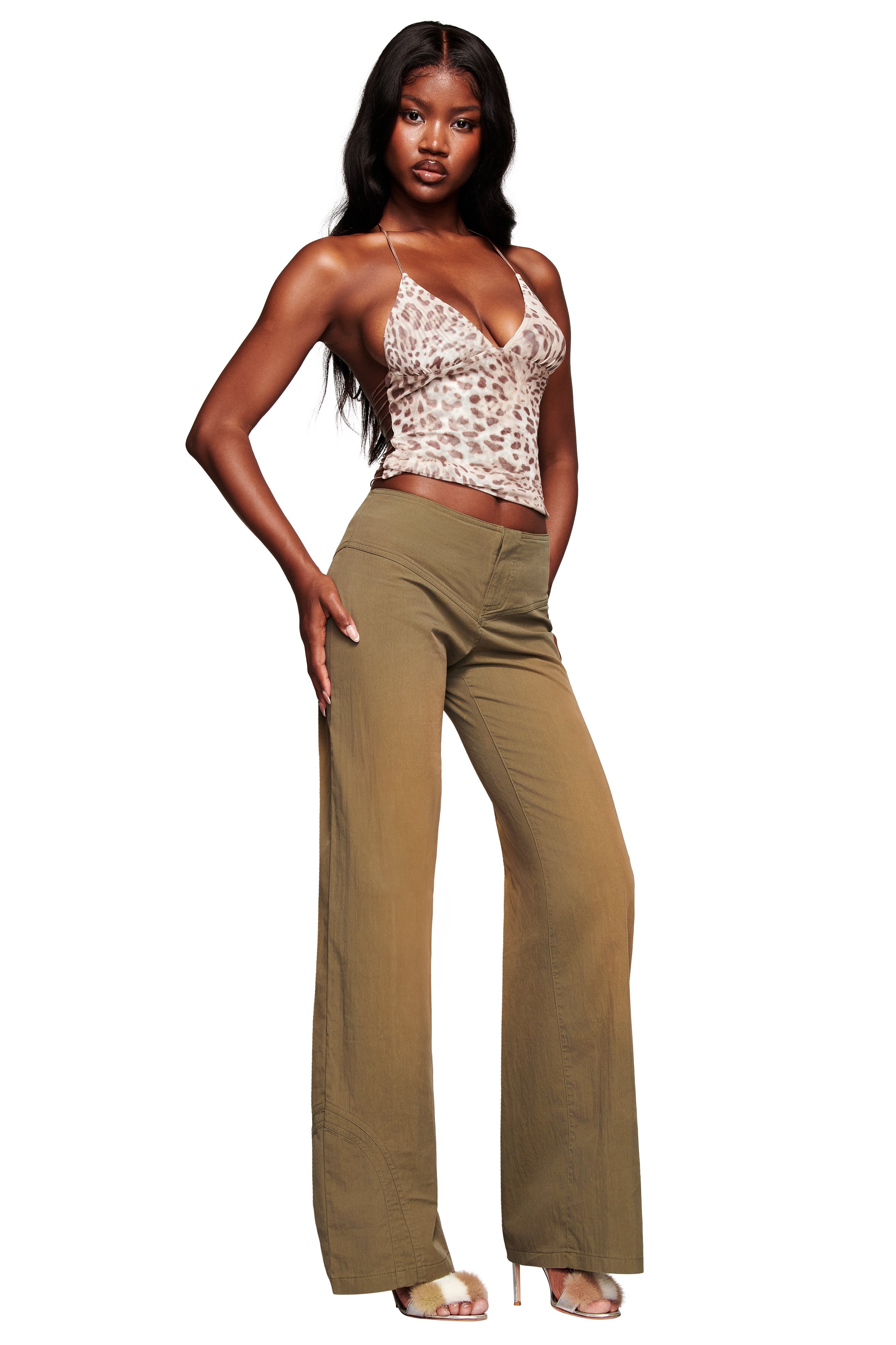 A woman stands confidently against a white background wearing the I.AM.GIA ELLERY TOP in leopard print, wide-leg olive green pants, and nude high-heeled sandals.