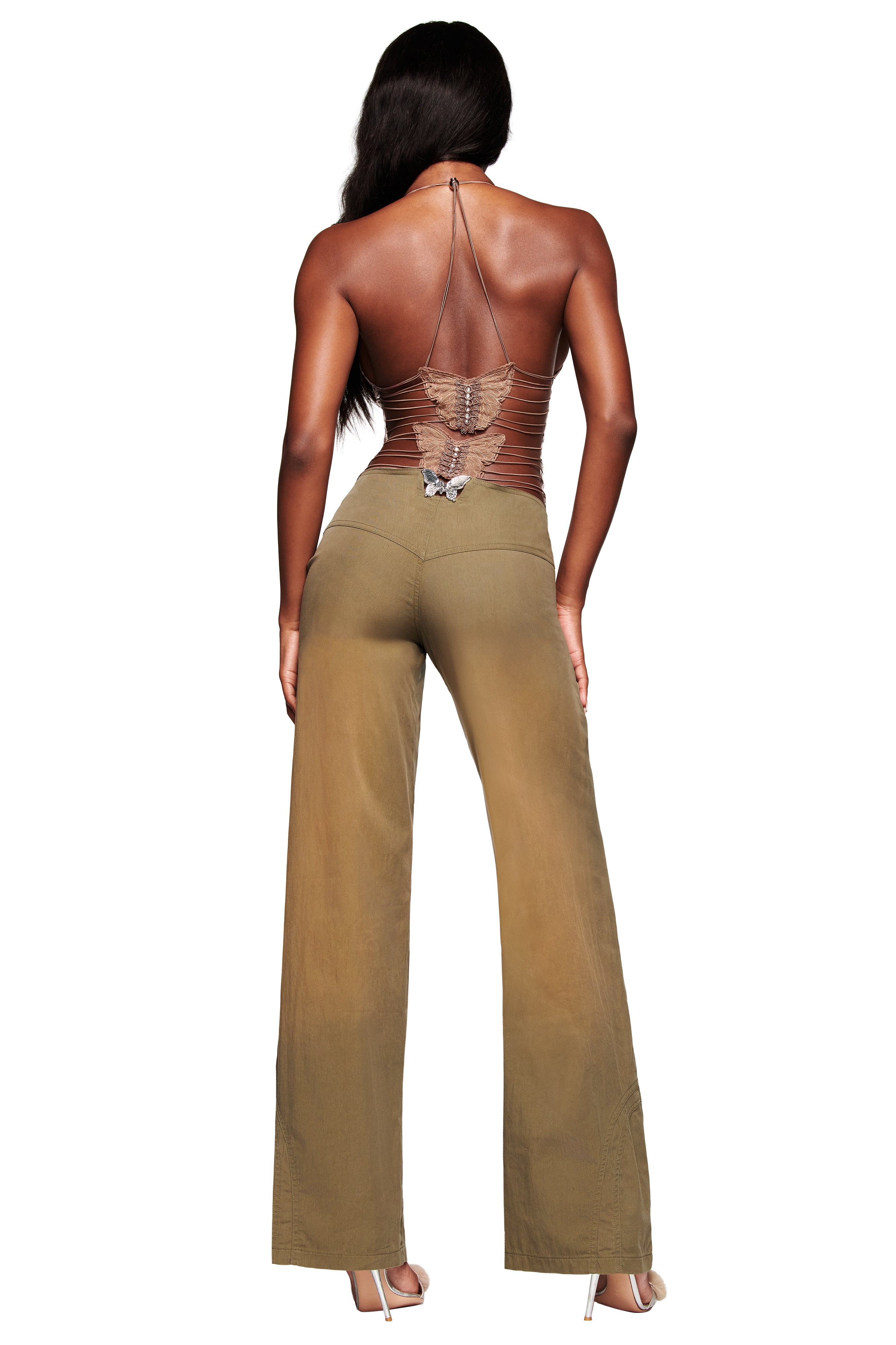 A woman with long wavy dark hair faces away, wearing I.AM.GIA's ELLERY TOP - LEOPARD, paired with olive wide-leg pants and high-heeled shoes.