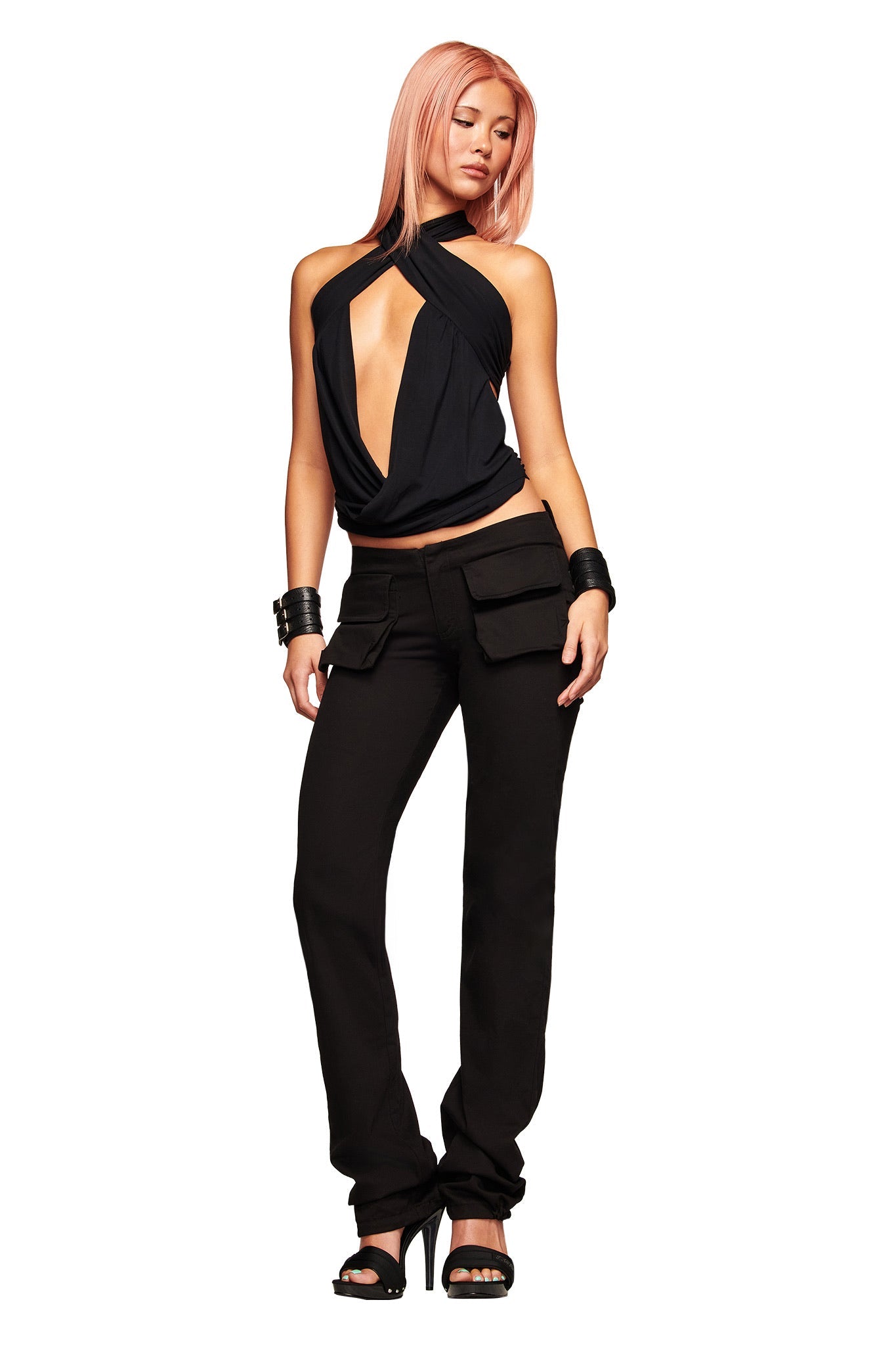 A woman with pink hair wears the I.AM.GIA SERREN TOP - BLACK, paired with black cargo pants, high heels, and bracelets, standing against a white background.