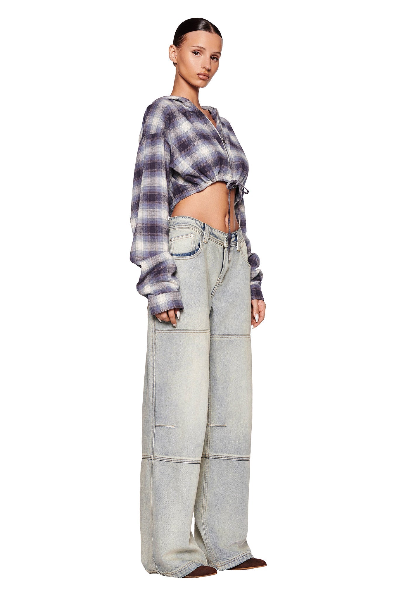 A model is posing against a white background, wearing an I.AM.GIA TIFF JACKET in blue with drawstring detailing and high-waisted, oversized light-wash jeans with visible stitching. She has her hair slicked back and gazes forward with her hands relaxed by her sides.