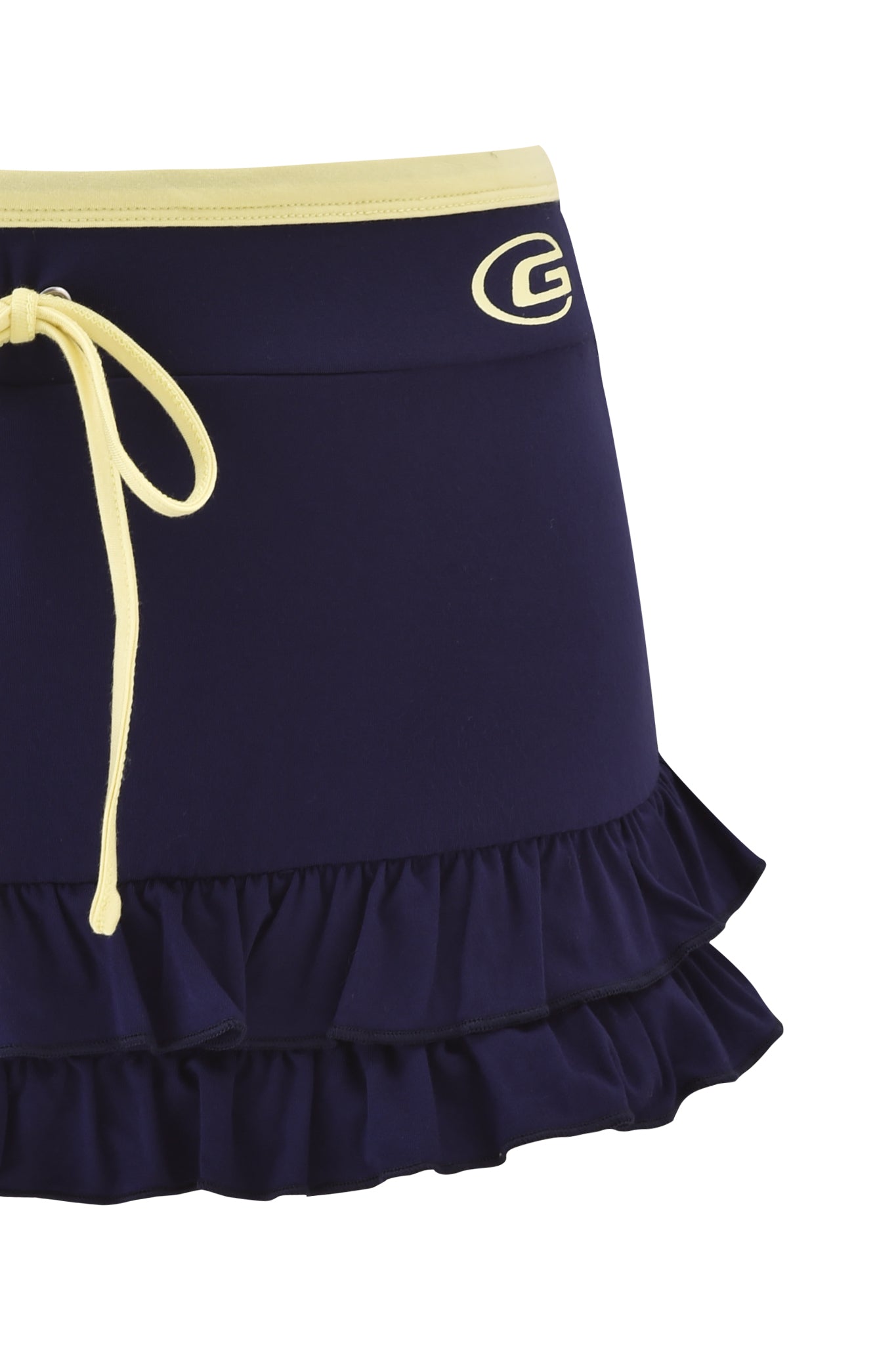 The MICHELLE SKORT - NAVY by I.AM.GIA is a navy blue micro mini skort with a yellow waistband and drawstring, white "G" logo on the side, and a playful ruffle hem.