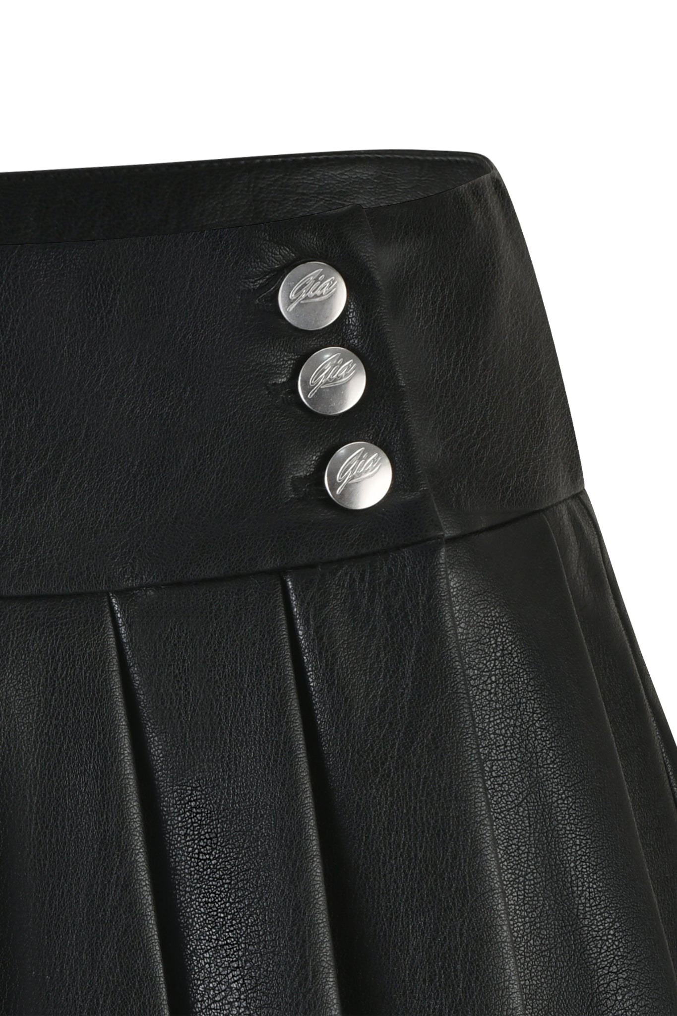 A close-up of the REMINI PU SKORT - BLACK from I.AM.GIA, showcasing a pleated design with three silver buttons on the waistband. The buttons feature an inscribed cursive logo.