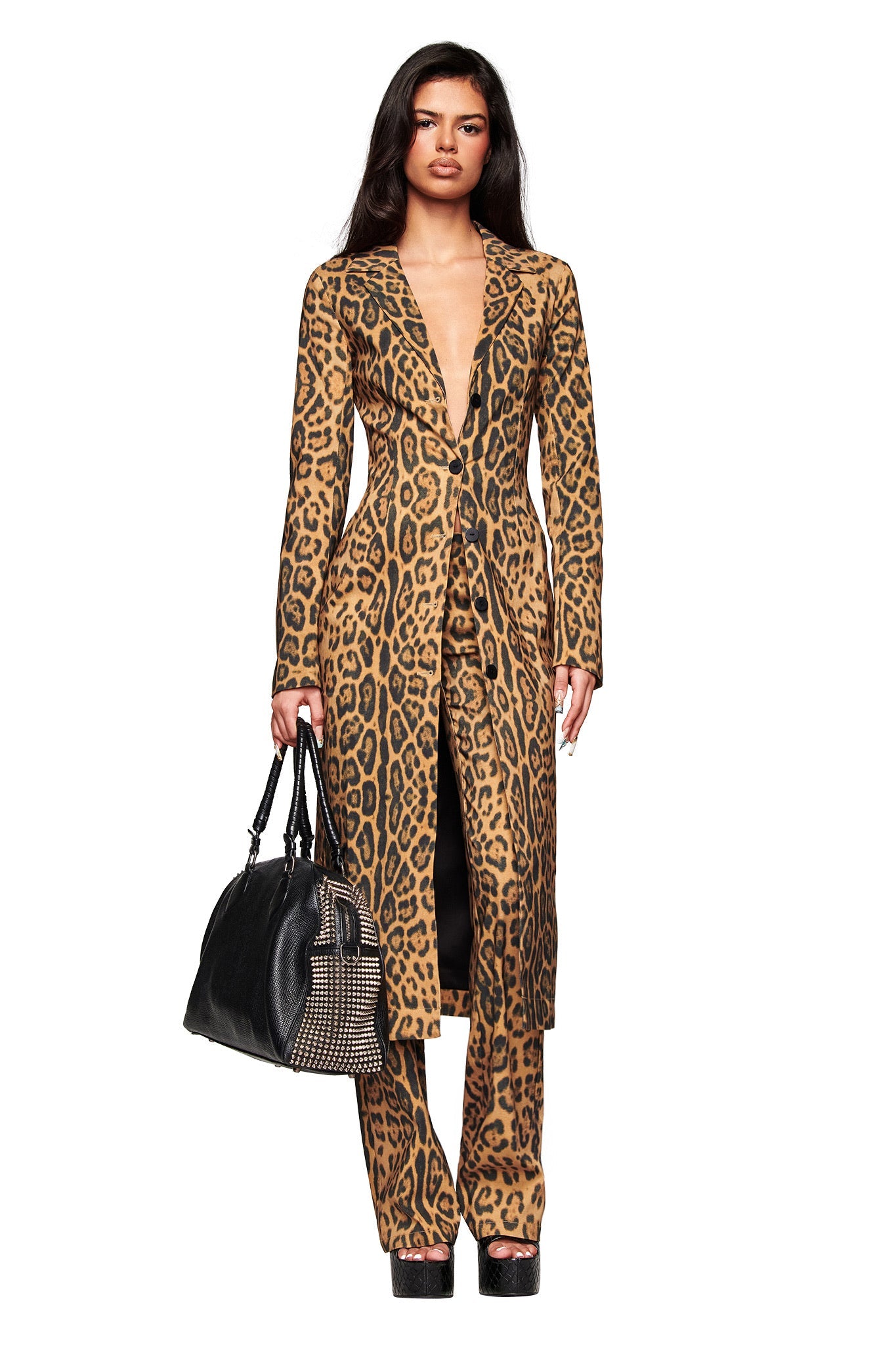 A woman poses against a white background wearing the I.AM.GIA UMA COAT - PANTHERA with matching pants, paired with a large black handbag and black platform shoes.