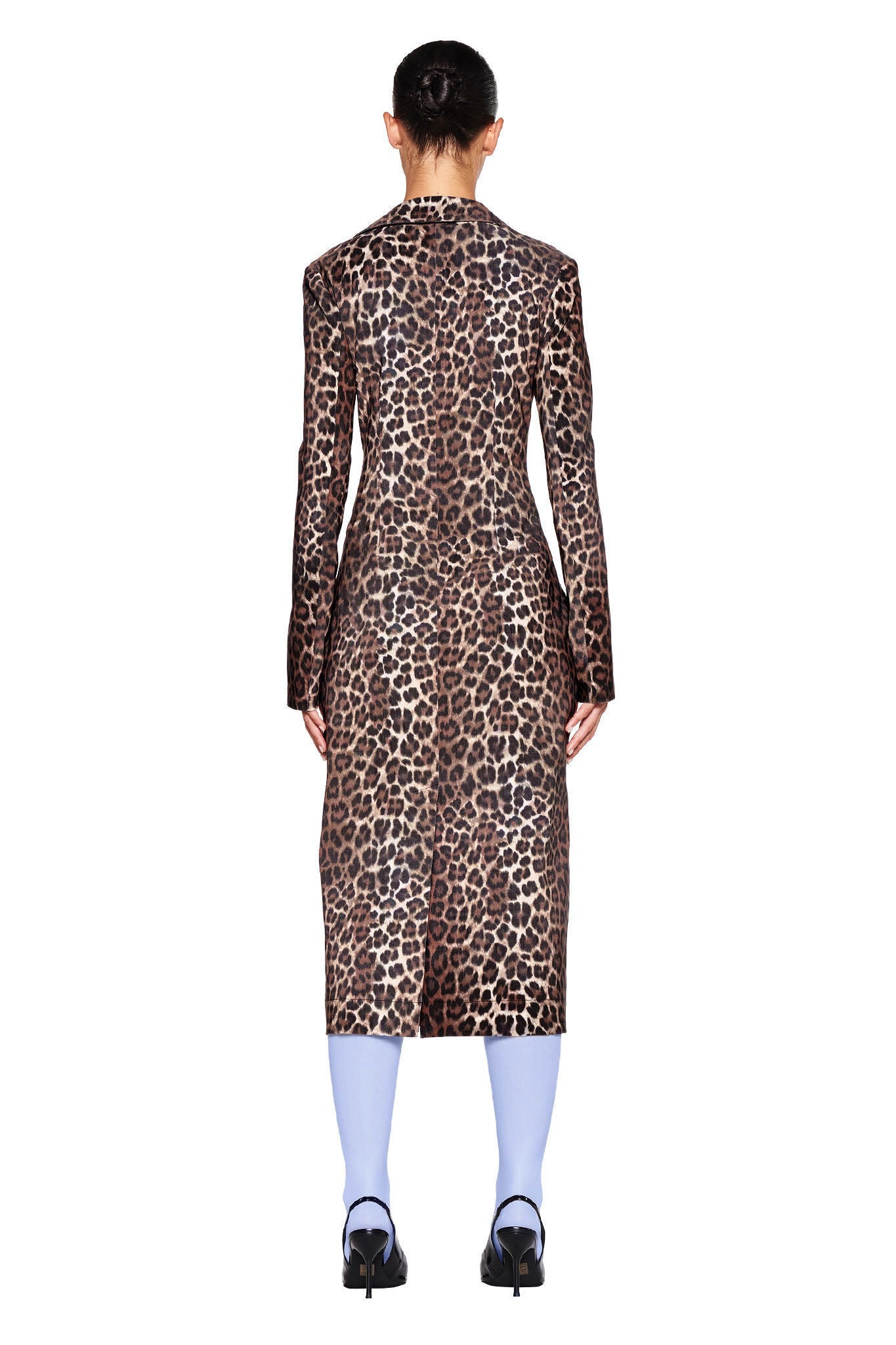 Rear view of a person in the UMA COAT - NEUTRAL : LEOPARD by I.AM.GIA. The person has a bun hairstyle and is paired with light blue tights and black high-heeled shoes. The leopard print coat falls to the knee, creating a striking contrast against the plain white background.