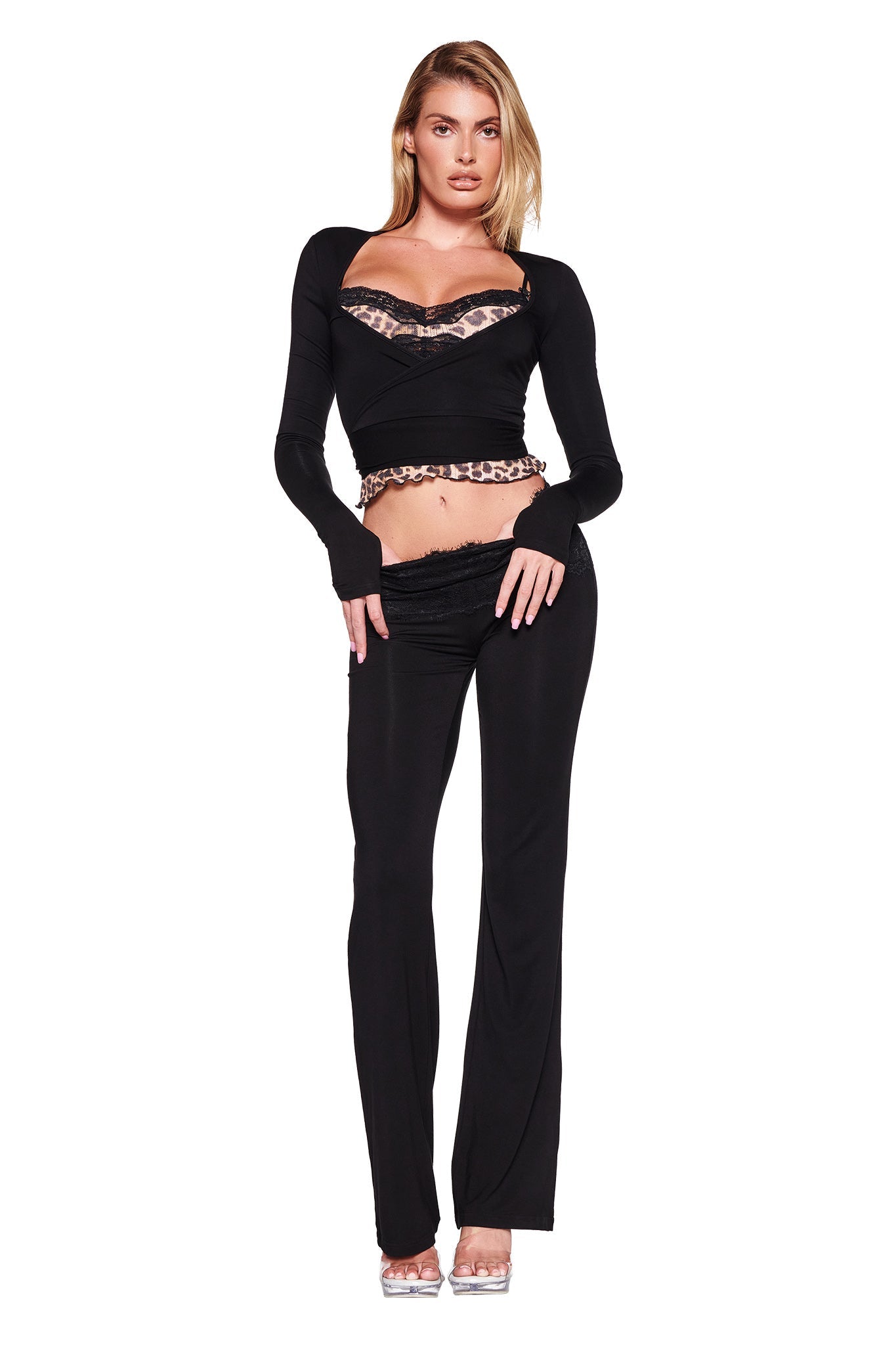 A model poses wearing the MANDY TOP - BLACK by I.AM.GIA, a stylish wrap top featuring lace and leopard print details. She pairs it with fitted black pants that highlight a bodycon silhouette. With one hand touching her waist and the other resting by her side, she exudes confidence in the super soft stretch bamboo fabric of the ensemble.