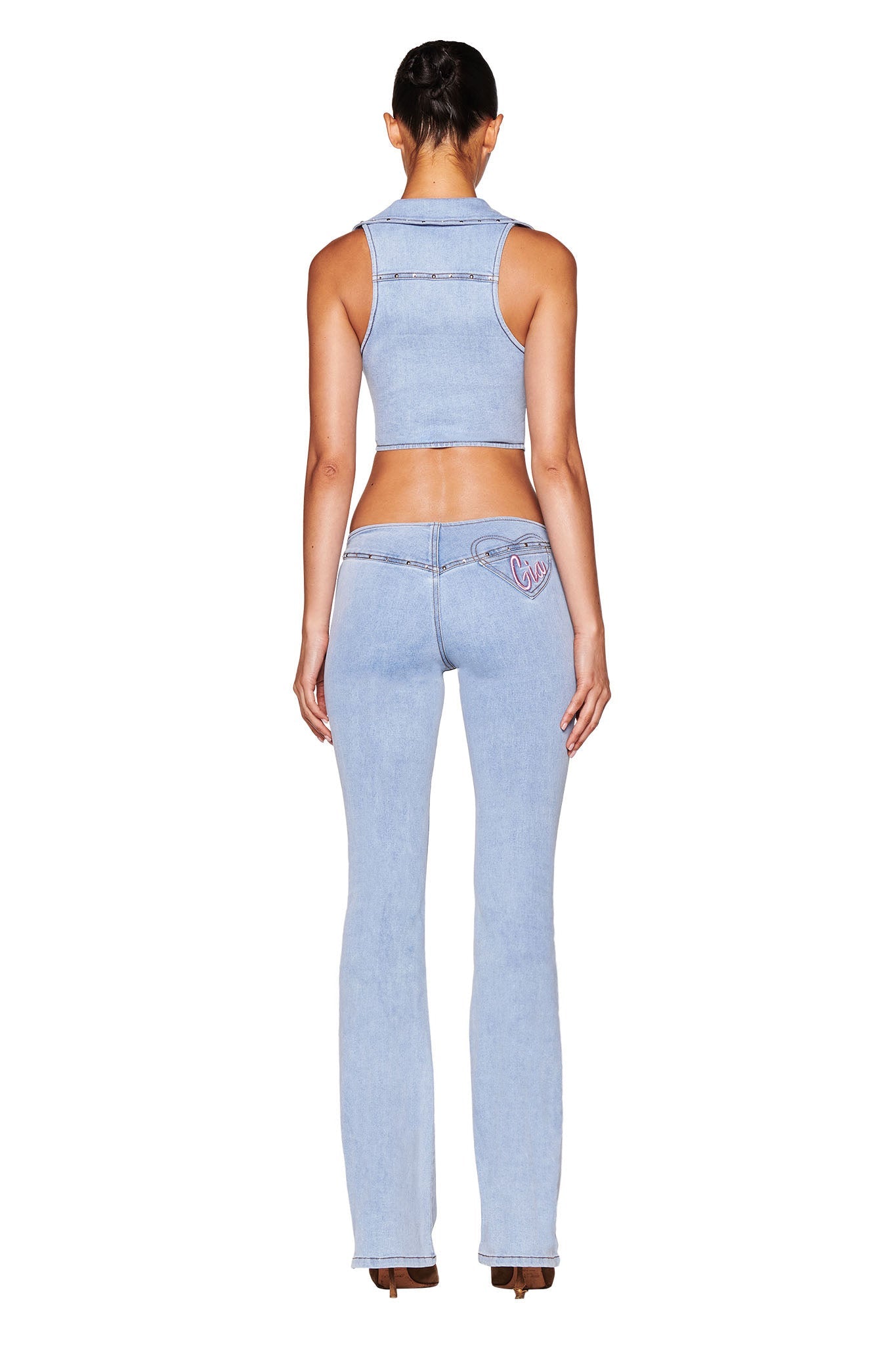 A person wearing a sleeveless denim top and I.AM.GIA's CARA JEAN - BLUE : LIGHT WASH with a heart-shaped pocket stands facing away. The fitted outfit features flared legs, set against a plain white background.