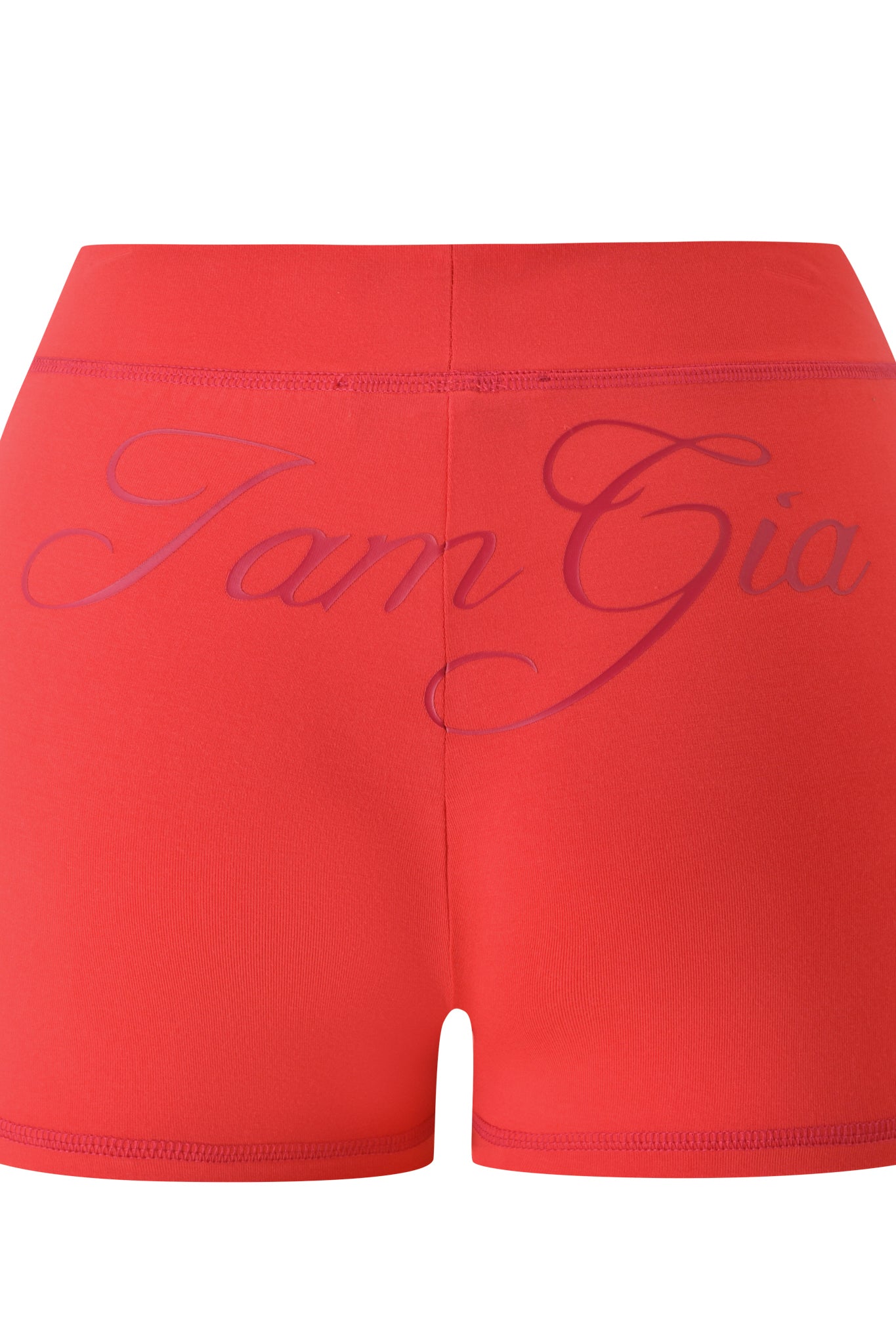 The BLARE SHORT - PAPAYA by I.AM.GIA is a red high-waisted short with an elastic waistband and bold purple "I.AM.GIA" cursive lettering across the back.