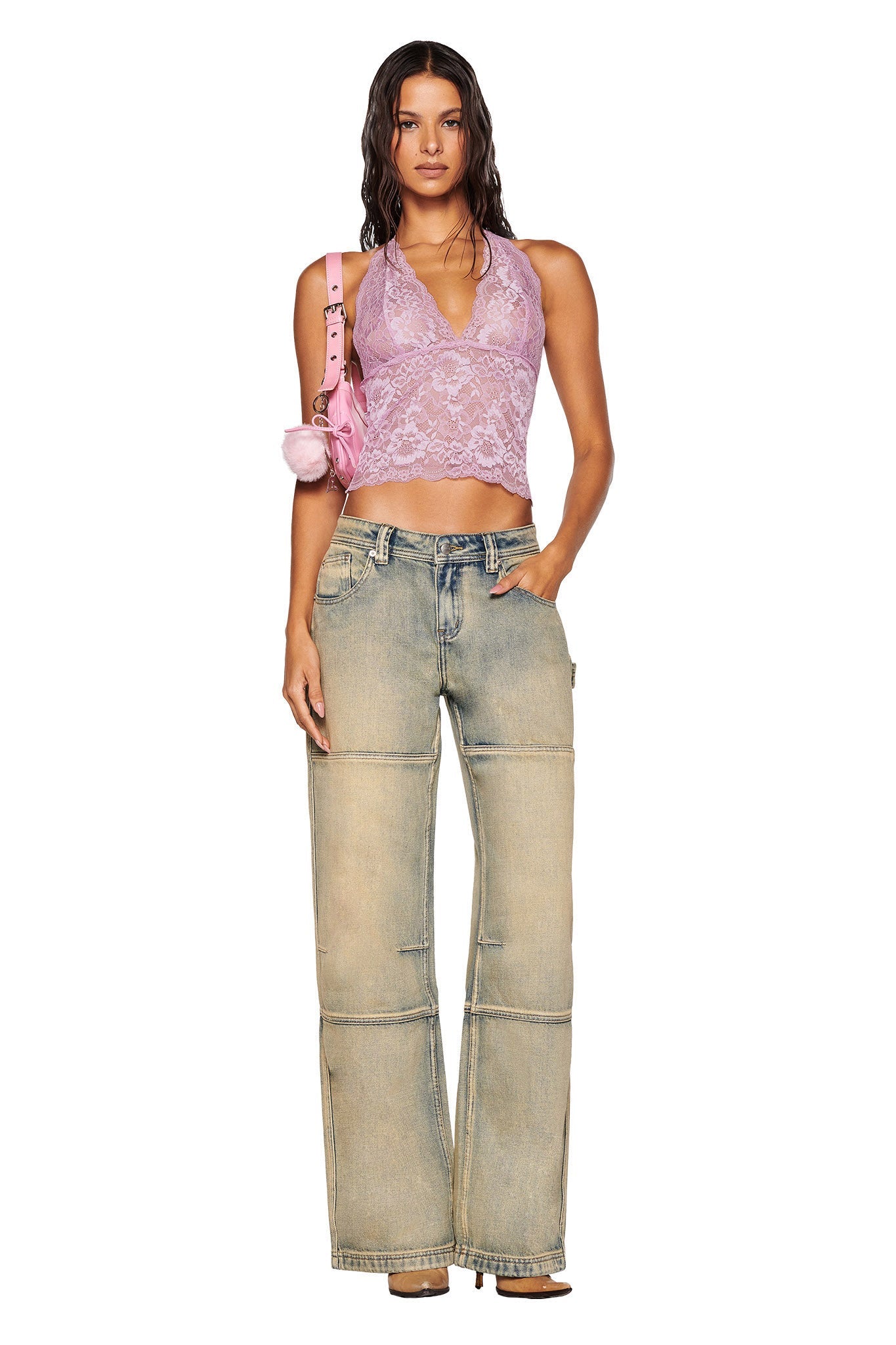 A person stands confidently, dressed in the I.AM.GIA GEM Halter Top in Lilac and wide-legged denim jeans. They hold a pink bag with a fluffy accessory against a plain white background.