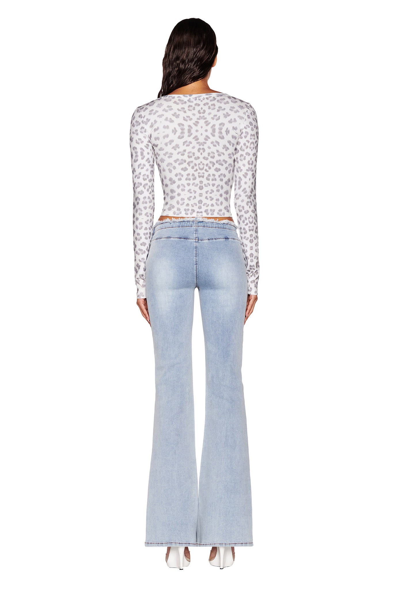 A person with long hair is wearing the PIPPA TOP in the SNOW LEOPARD colorway from I.AM.GIA's WINTER WILD CARD collection and light blue flared jeans, standing against a plain white background with their back to the camera.