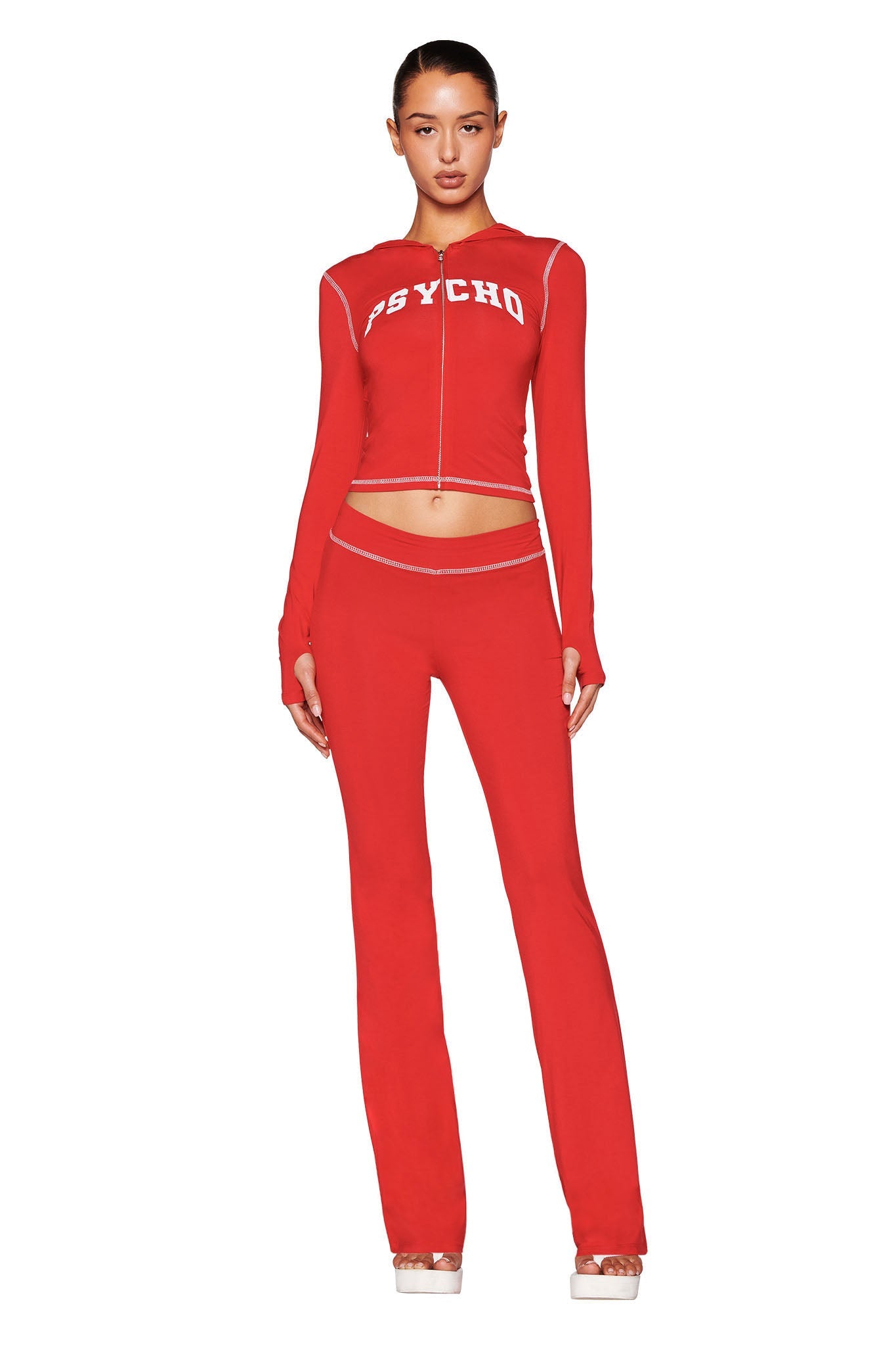 A woman faces forward in a red fitted long-sleeve "PSYCHO" top and I.AM.GIA BLARE TRACKPANT - RED: PSYCHO : SALSA low-rise trackpants with cut-out waist details. Her hair is pulled back, and she wears platform shoes.