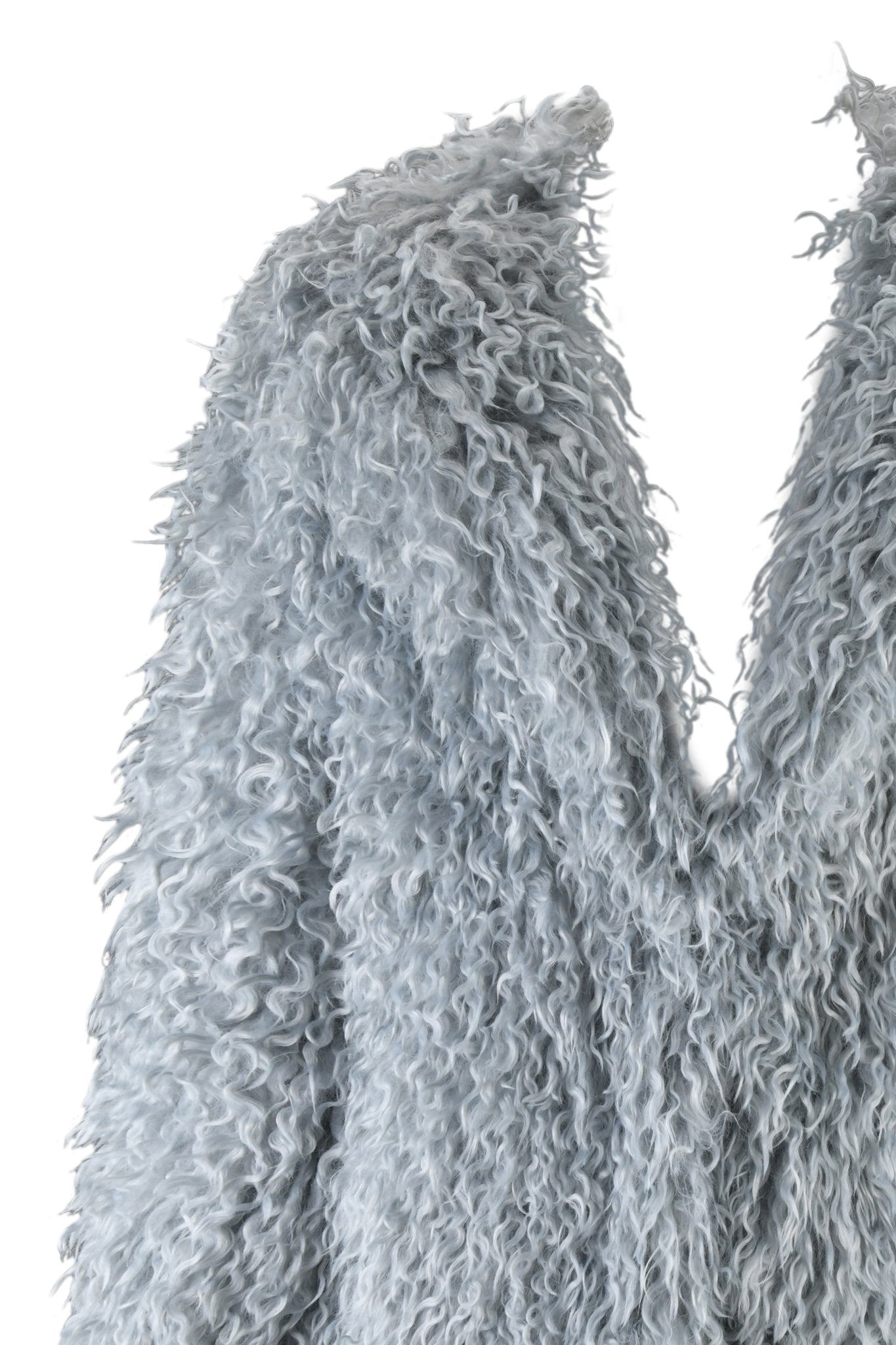 A close-up of the I.AM.GIA ARAMINTA COAT in a light blue, curly faux Mongolian sheepskin material fills the frame with its textured appearance against a plain white background. The fabric looks soft and fluffy, suggesting an oversized fit perfect for cozy elegance.