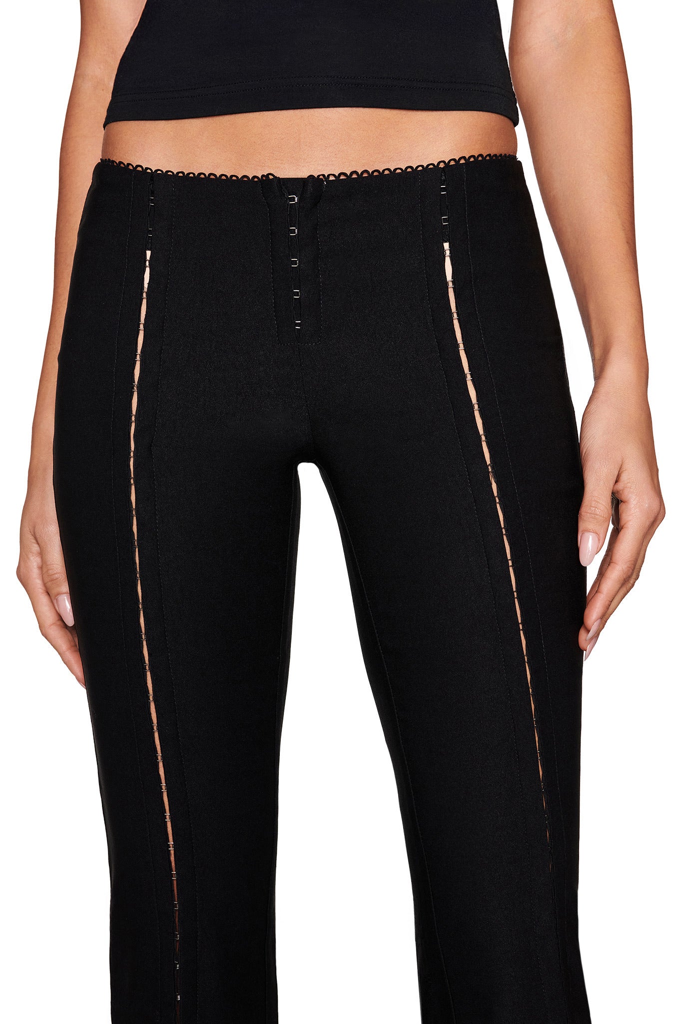 Someone is wearing I.AM.GIA's RONAN PANT - BLACK, featuring hook-and-eye detail and vertical lace-up design. The upper body is partially visible against a white background.