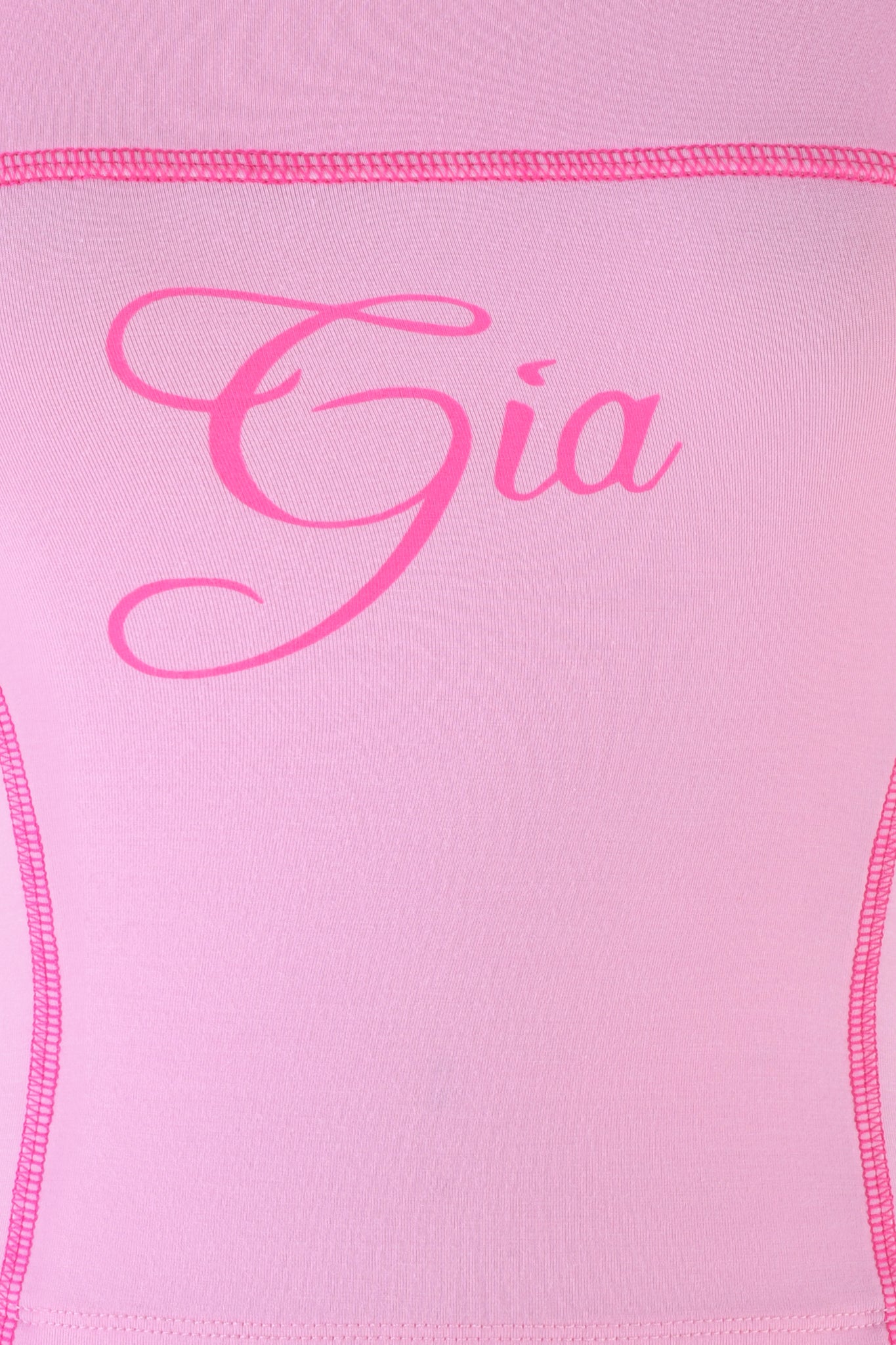 Zoomed-in image of the pink fabric from the BLARE BOOB TUBE - PINK : BUBBLEGUM by I.AM.GIA, showing the "Gia" logo in elegant hot pink cursive and contrast stitching along the edges, suggesting it's part of a garment.