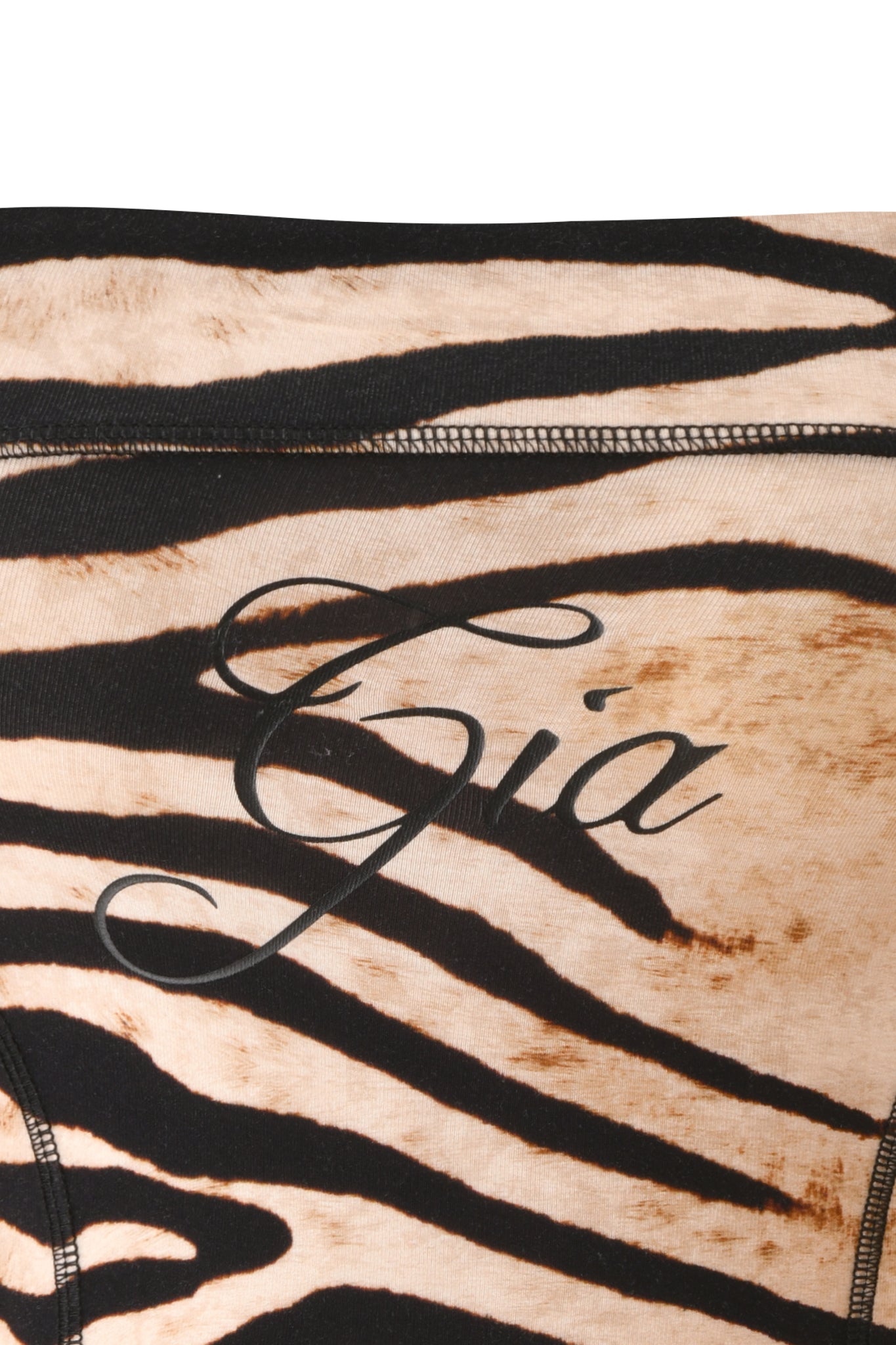 Close-up of fabric with a tan and black zebra pattern, featuring sporty princess seams and the word “Gia” written in black cursive lettering across the center, capturing the distinctive style of the I.AM.GIA BLARE BOOB TUBE - WILD SIDE.