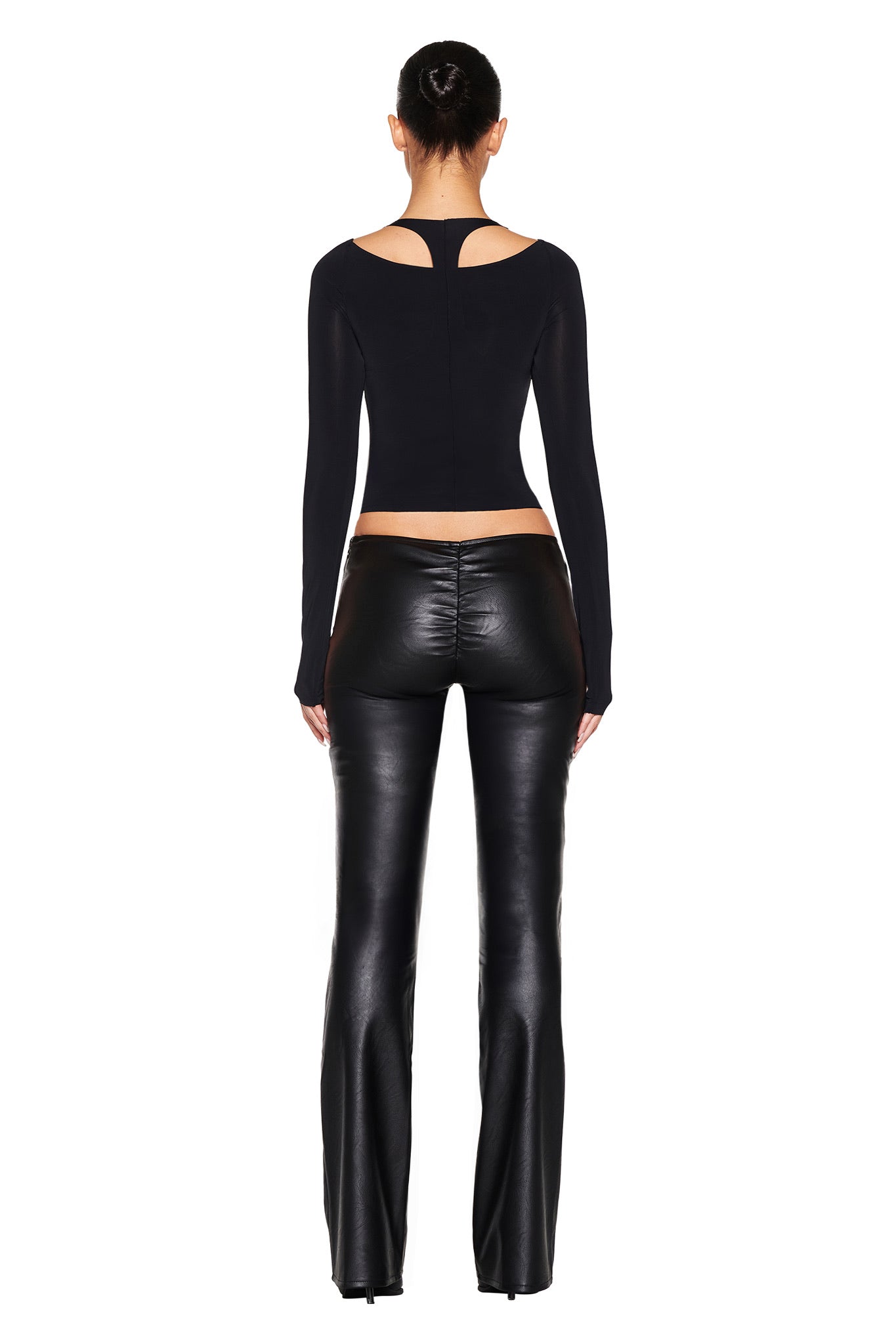 Rear view of a person with hair up, wearing a fitted I.AM.GIA NERINA LONG SLEEVE TOP - BLACK and flared black leather pants, standing against a plain white background.