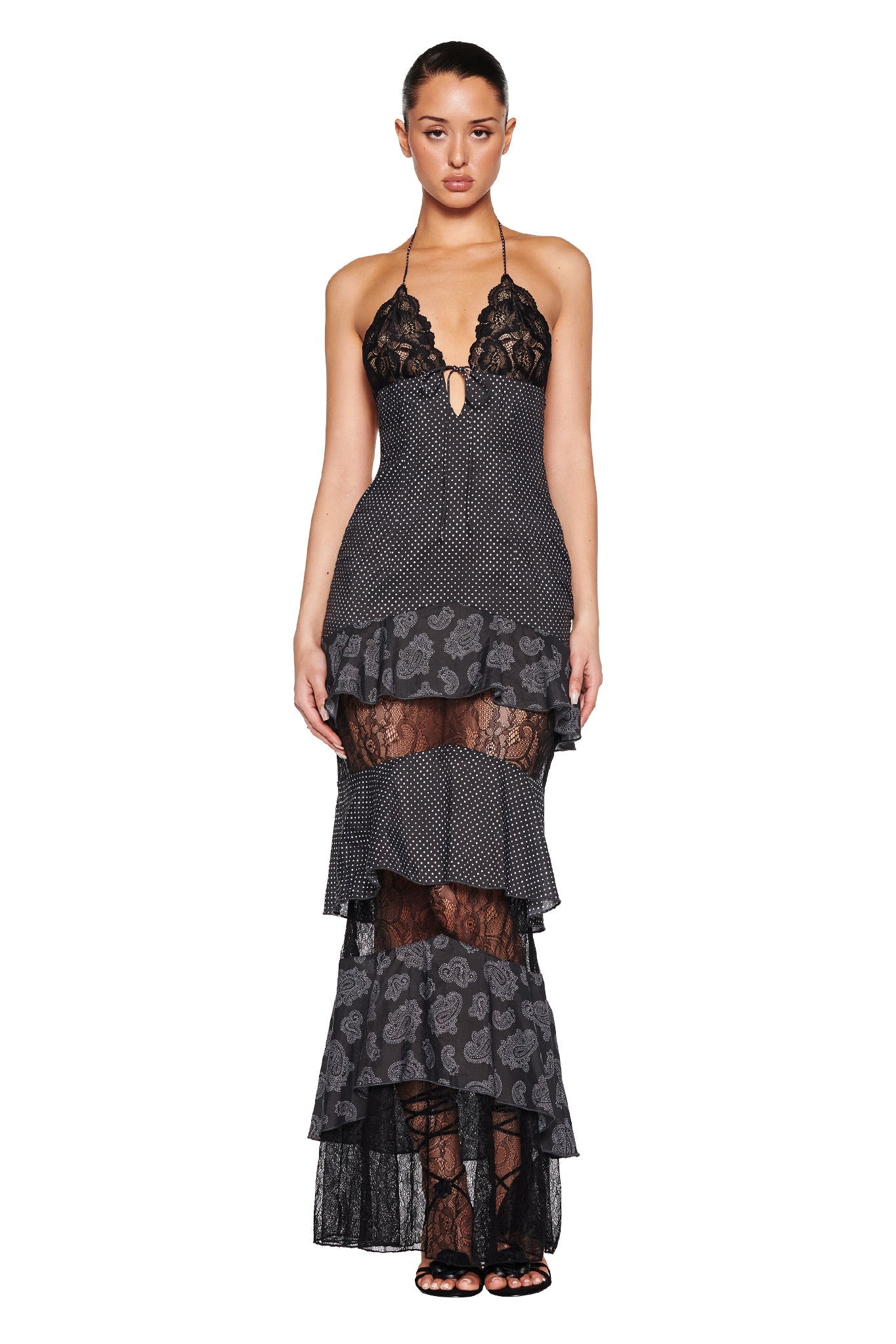 A woman poses against a white background in the I.AM.GIA PEARL MAXI DRESS - BLACK: POLKA DOT, featuring a tiered silhouette with lace panels, sheer polka dot details, a halter neck, keyhole bust opening, and mermaid hem.