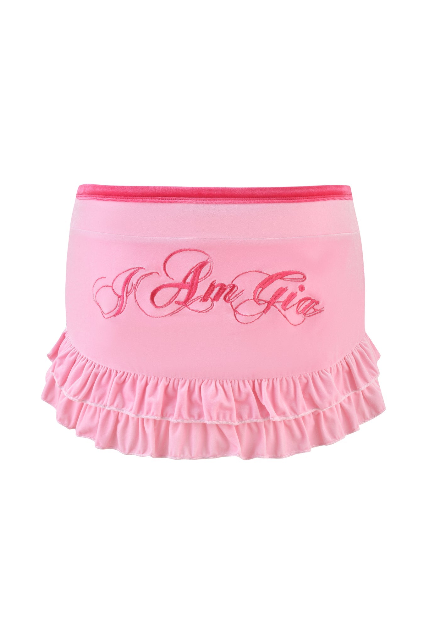 The MICHELLE VELOUR MINI SKORT by I.AM.GIA is pink with "I Am Gia" in cursive on the front, featuring a ruffled hem and low-rise waist, set against a white background with a dark pink waistband.