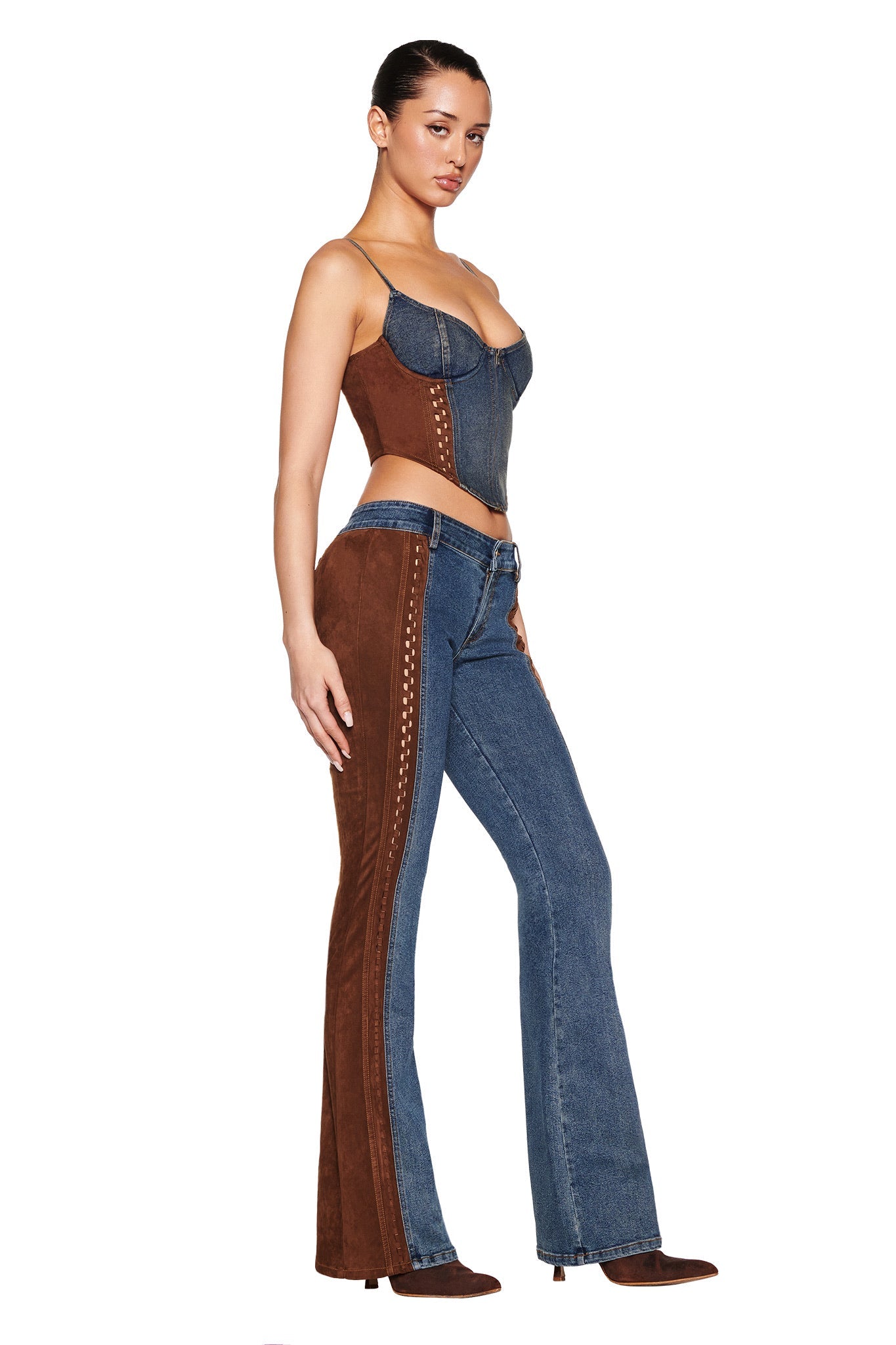 A woman poses in the FORREST PANT - BLUE: MEDIUM WASH from I.AM.GIA. She wears a sleeveless, form-fitting top with a sweetheart neckline and matching flare jeans with brown suede contrast side panels. Her hair is pulled back as she stands against a plain white background, embracing the vintage washed effect.