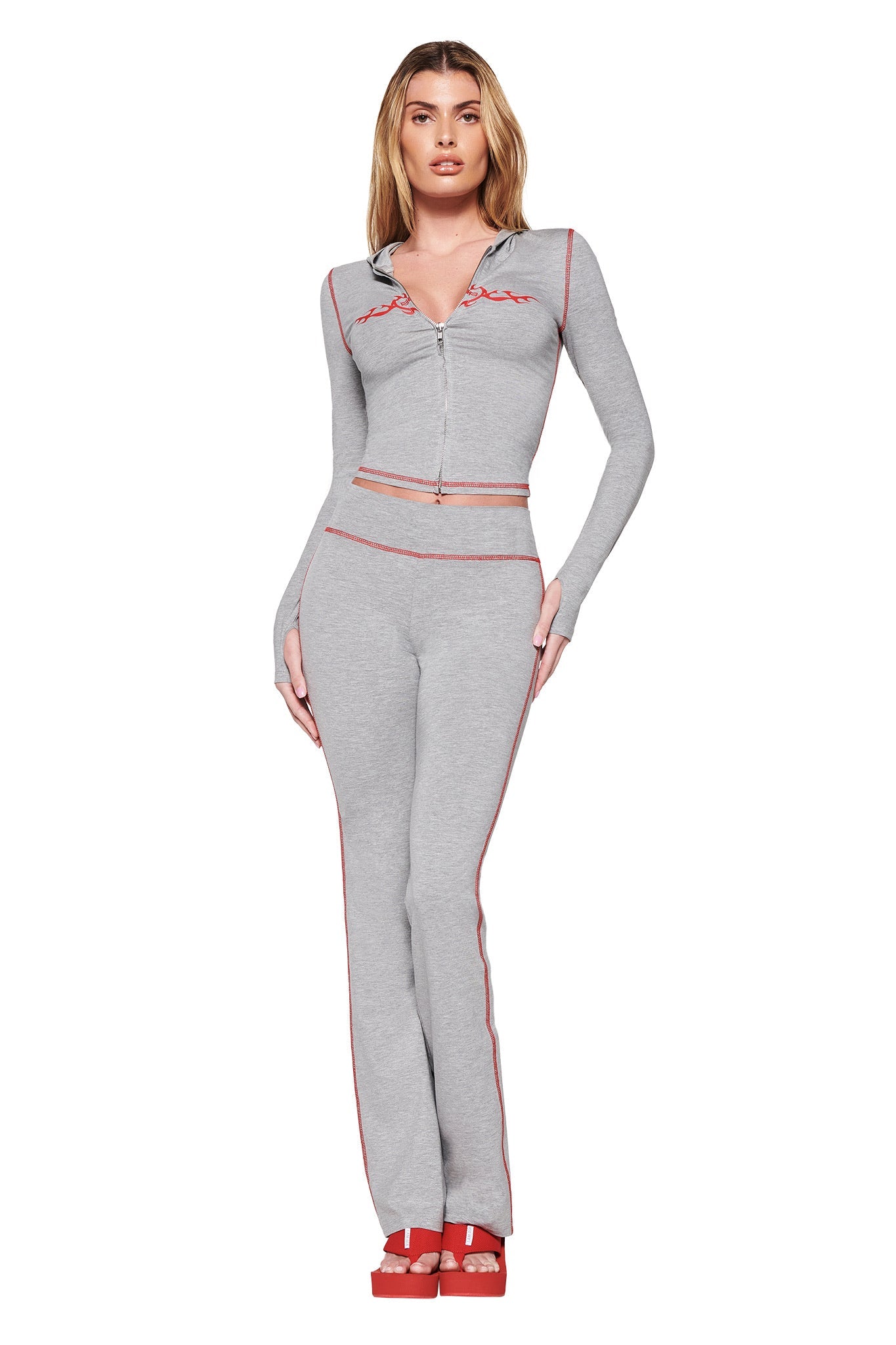 Dressed in the sleek BLARE HOODIE - GREY from I.AM.GIA, paired seamlessly with fitted bodycon pants and red heels, a person stands confidently against a white background.