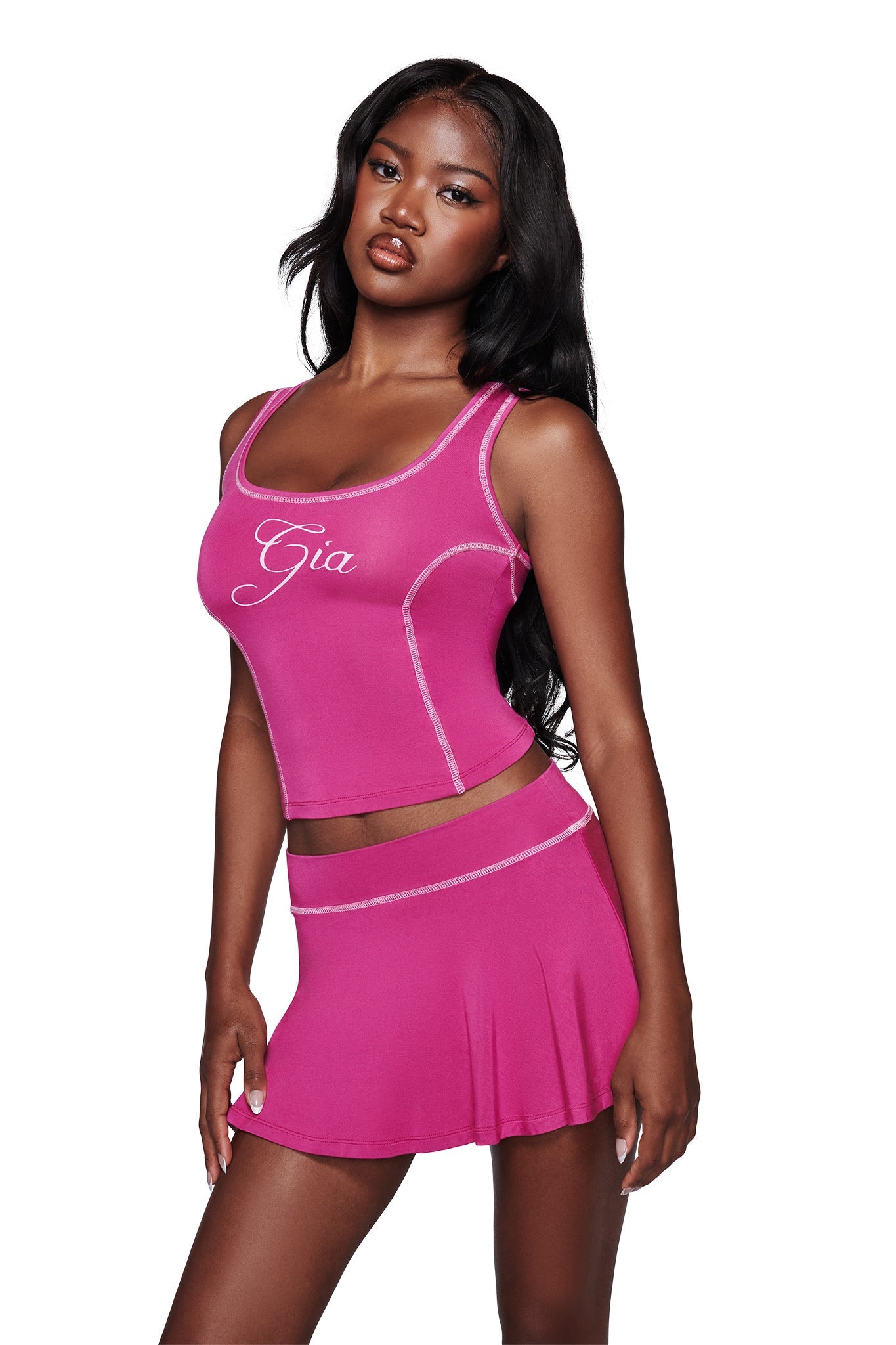 A woman wears a bright pink sleeveless crop top with "Gia" on it and the I.AM.GIA BLARE SKORT in raspberry, posing against a white background.