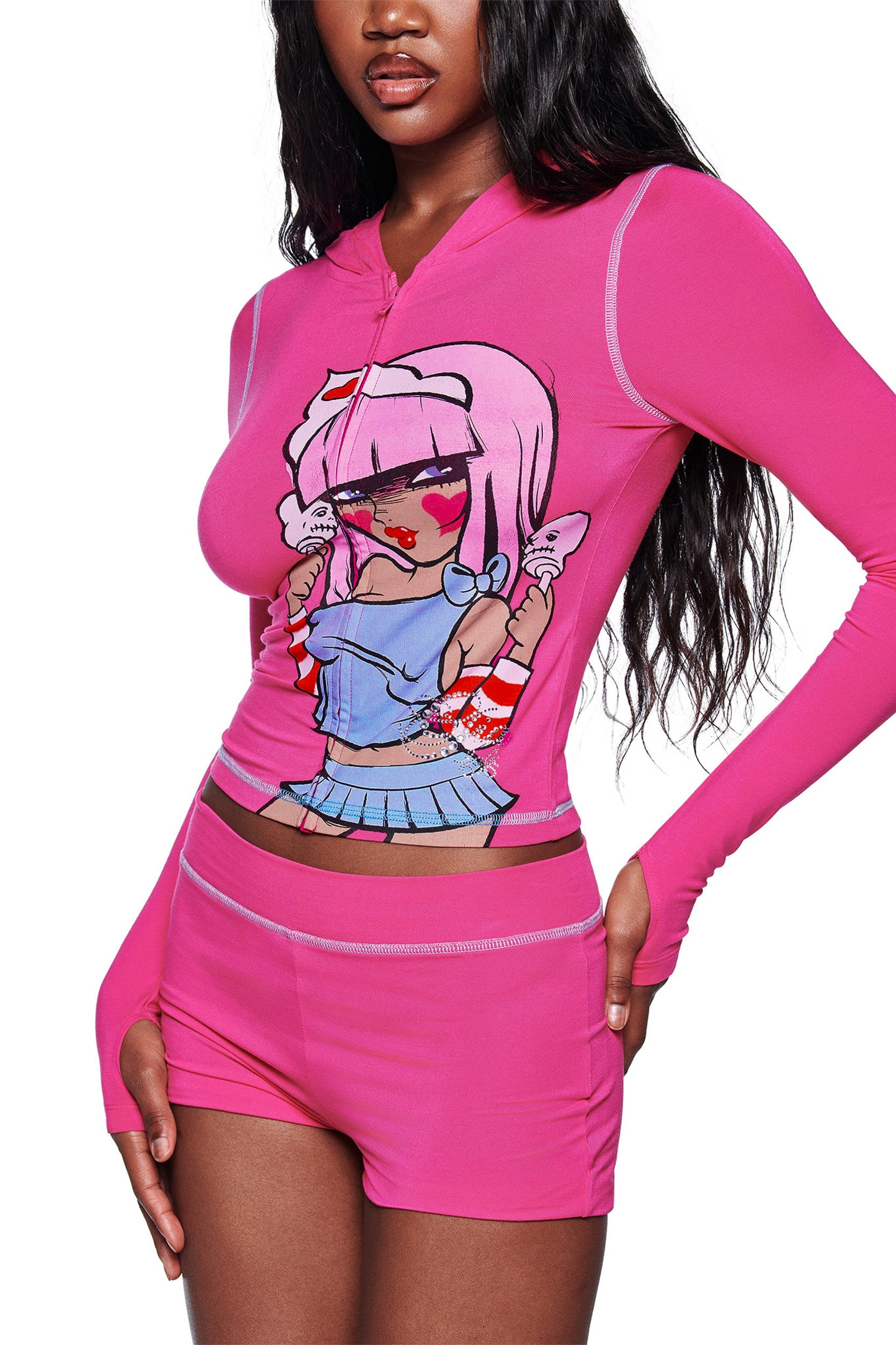 A woman wears the I.AM.GIA FAFI BLARE HOODIE in hot pink, featuring an anime-inspired graphic from the Fafi collaboration. She has one hand on her hip and her long hair is styled loose.