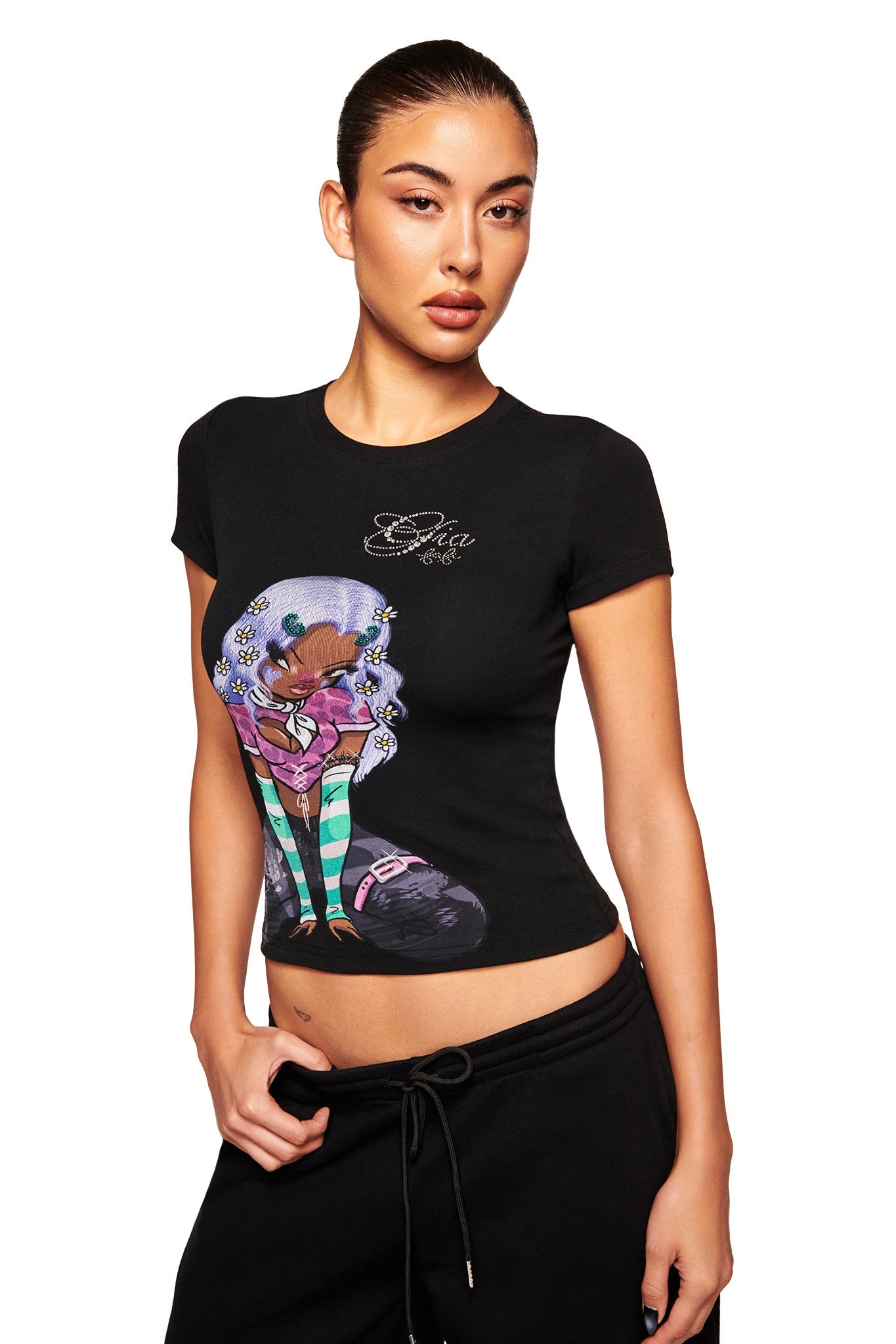 A woman with slicked-back hair wears the I.AM.GIA FAFI T-SHIRT in black, featuring an illustrated girl with purple hair, green striped stockings, and flowers, paired with black pants against a white background.