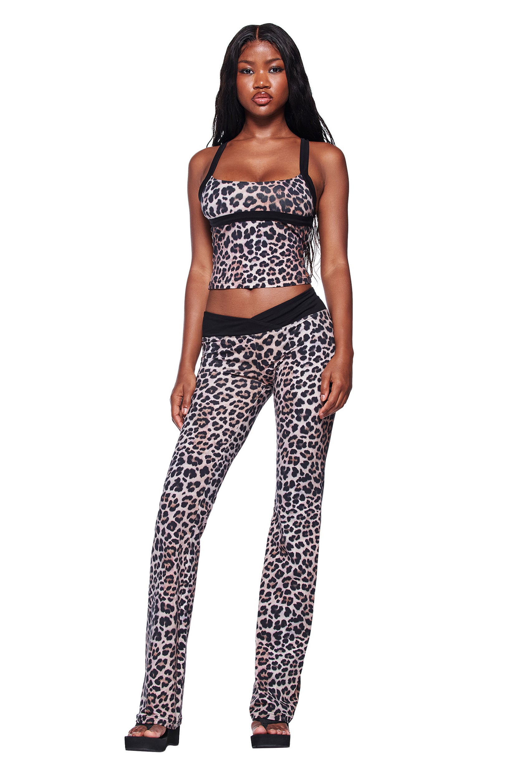 A woman faces forward wearing the I.AM.GIA BLARE HALTER STRAP TOP in leopard print with matching high-waisted pants featuring black accents and black platform sandals, set against a white background.