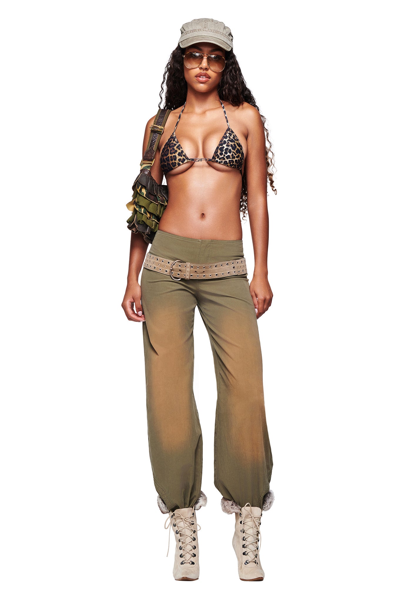 A woman wearing I.AM.GIA’s SEQUOIA PANT in army green, a leopard print bikini top, beige boots, a matching cap, sunglasses, and a military-style bag stands against a white background.