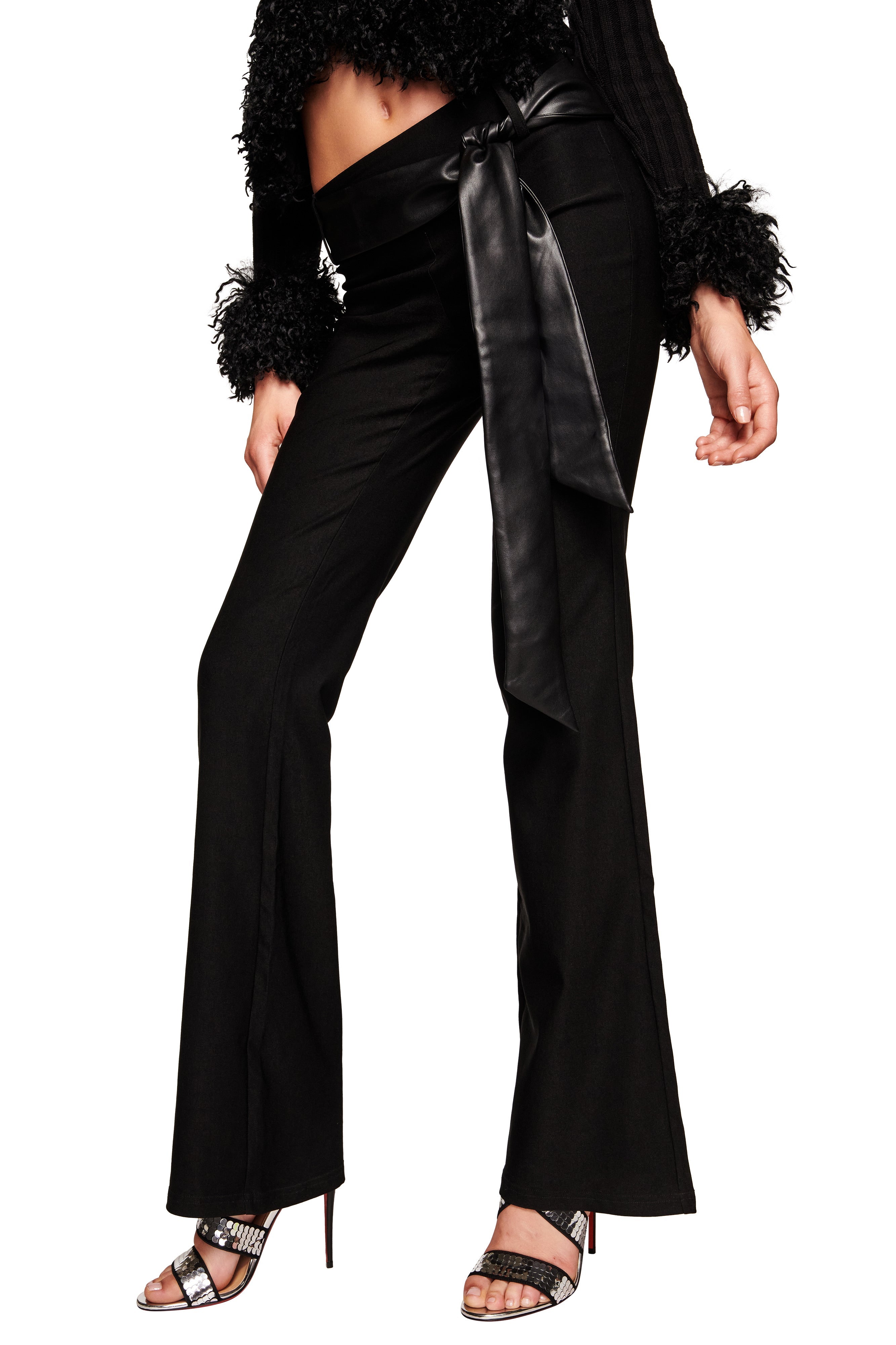 A person wears the I.AM.GIA FELIZ PANT - BLACK paired with a wide faux leather belt, cropped fuzzy black top, and black sandals with silver accents. The person's face is not visible.