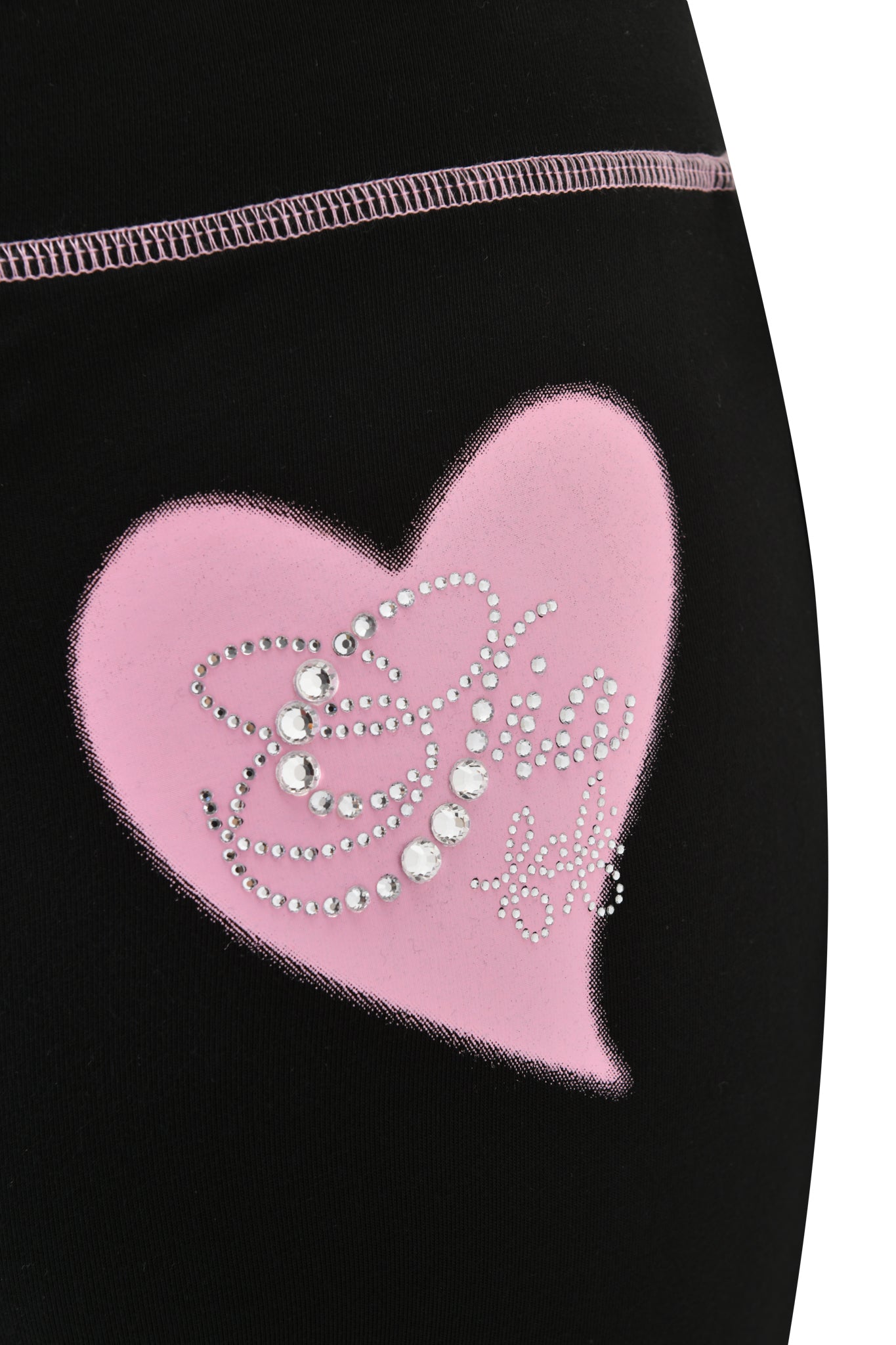 Close-up of I.AM.GIA FAFI BLARE PANT - BLACK fabric, featuring a large pink heart with shiny rhinestone accents forming partial words and visible pink stitching along the top seam.