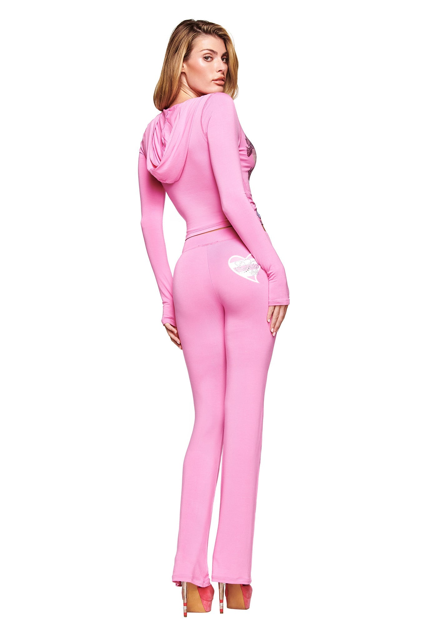 A woman models the I.AM.GIA FAFI BLARE PANT in bubblegum pink, featuring a white heart on the back pocket. She faces backward in heels, glancing over her shoulder in true Fafi collaboration style.