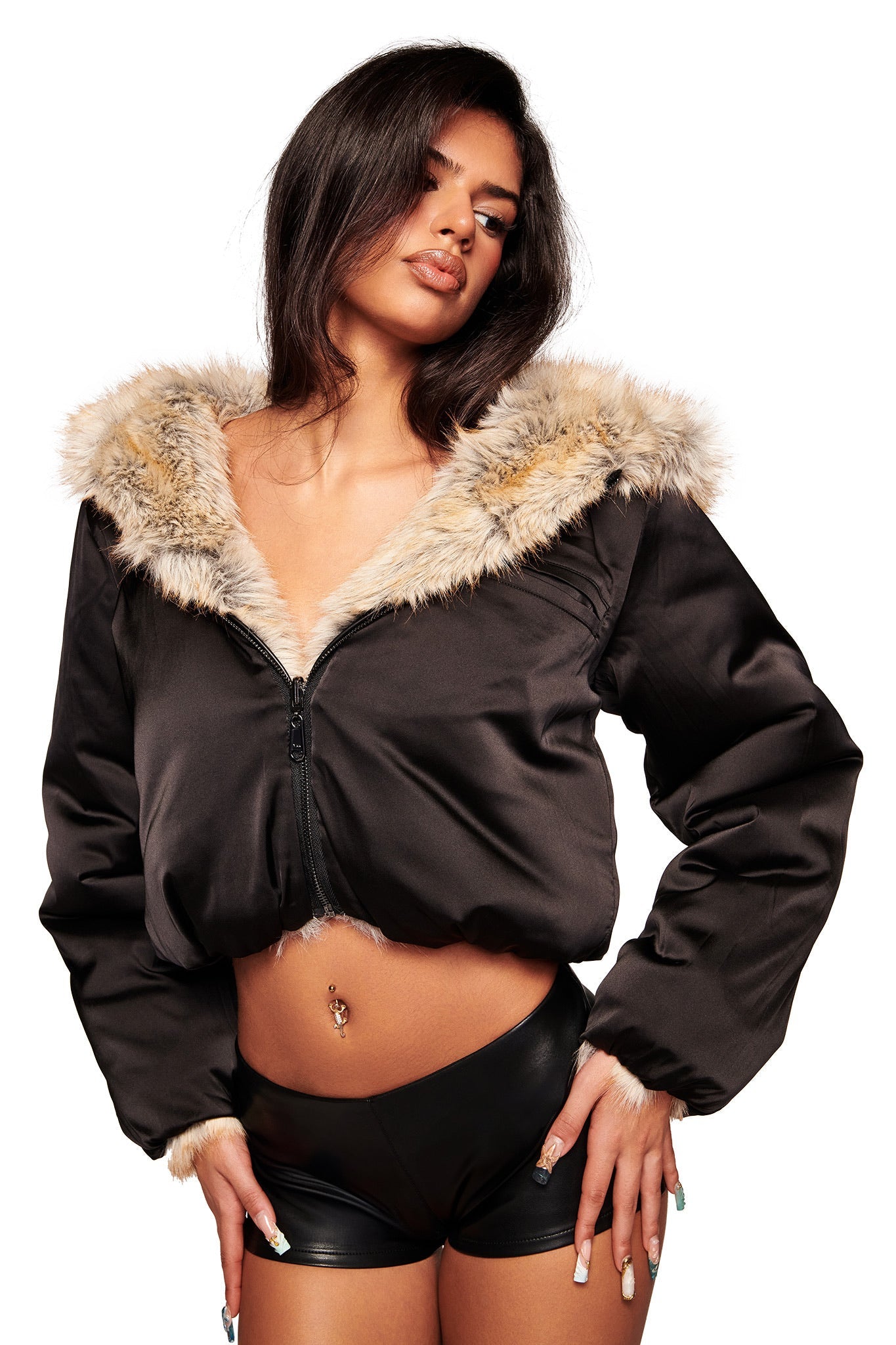 A woman with long dark hair and a belly button piercing wears the I.AM.GIA EVEREST REVERSIBLE JACKET in brown, styled with black high-waisted shorts, posing against a white background.