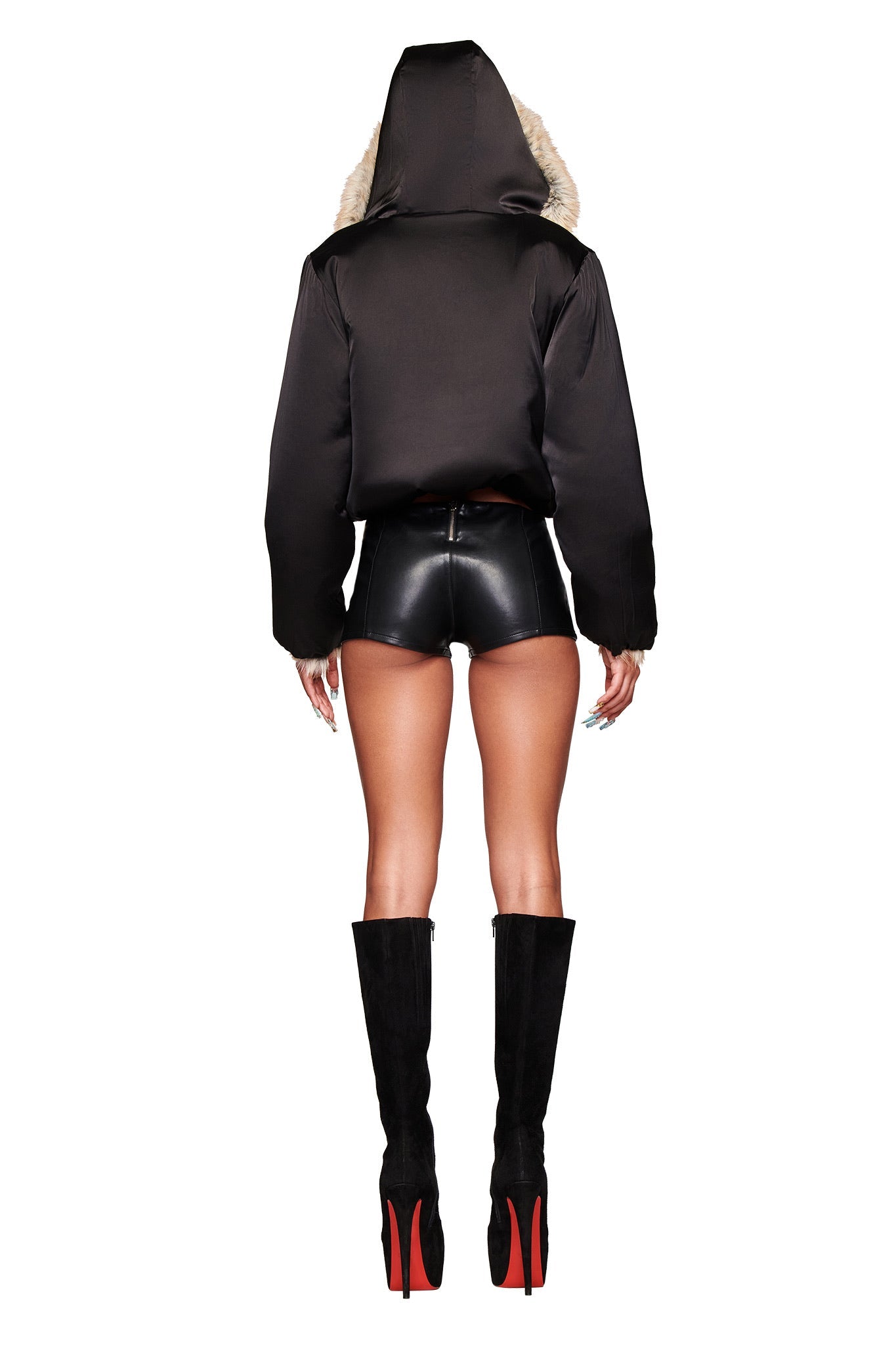 Wearing the I.AM.GIA EVEREST REVERSIBLE JACKET in brown, black leather shorts, and tall black boots with red soles, a person stands with their back to the camera against a white background.