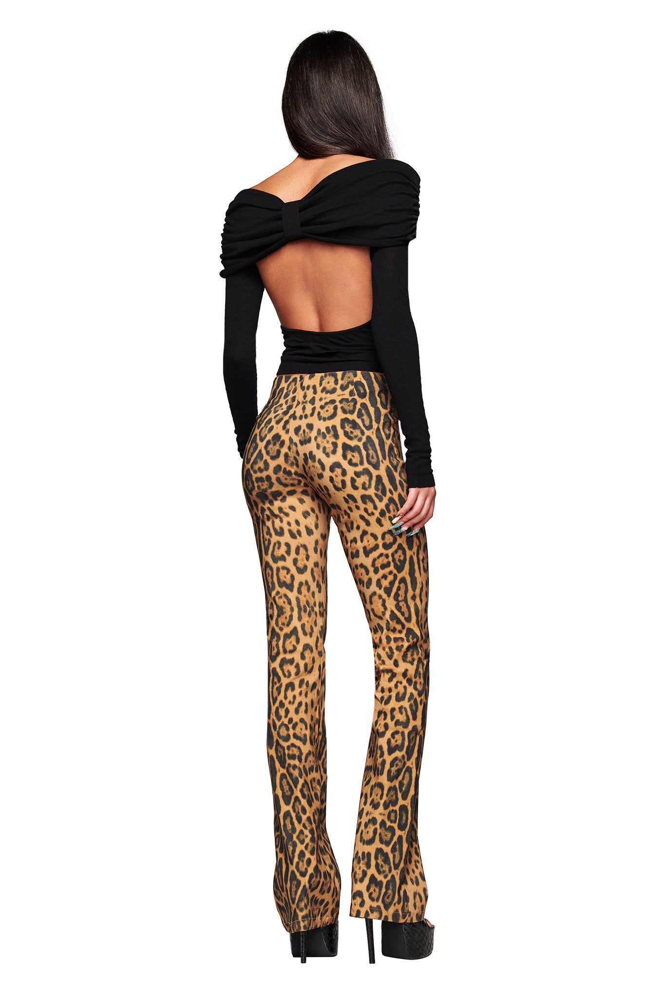 A woman faces away in a black open-back top with ruched shoulders and long sleeves, paired with I.AM.GIA's UMA PANT - PANTHERA high-waisted animal print flared pants and black platform heels.