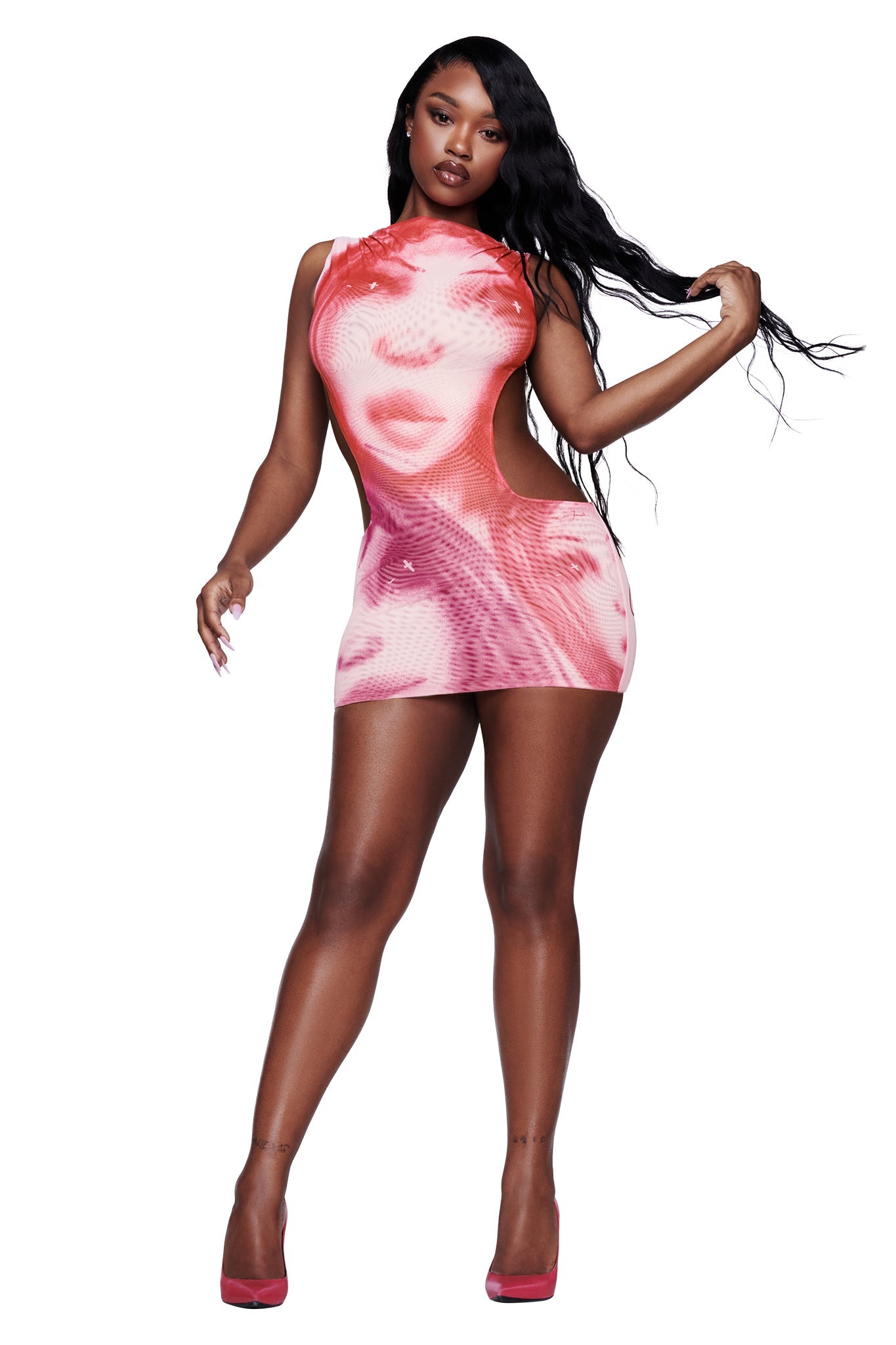 A woman poses in the I.AM.GIA T-REX CORALINE MINI DRESS - PINK, a sleeveless, form-fitting micro mini dress adorned with a bold pink-toned face graphic inspired by the brand’s signature print. She has long, wavy black hair and pairs the look with matching pink high heels, set against a white background.