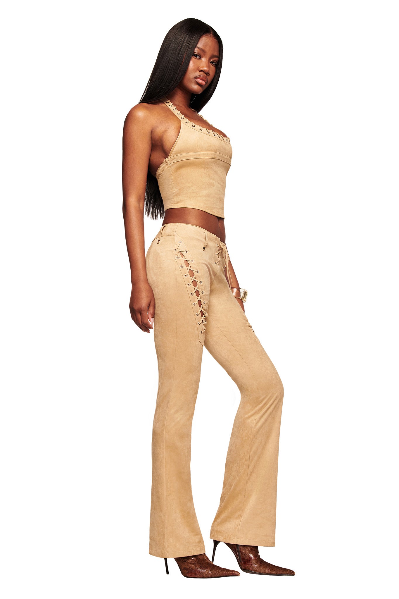 A woman poses in profile wearing I.AM.GIA’s XENIA SUEDE PANT - TAN with a matching suede crop top, pointed brown heels, and long straight hair against a plain white background.