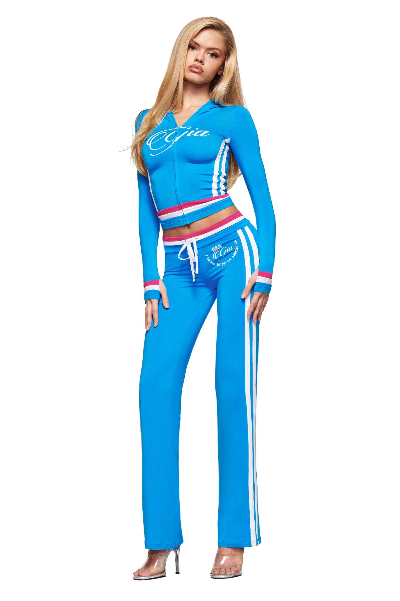 A woman with long blonde hair models the I.AM.GIA BLARE STRIPED HOODIE in sky blue, styled with matching pants and heels against a white background.