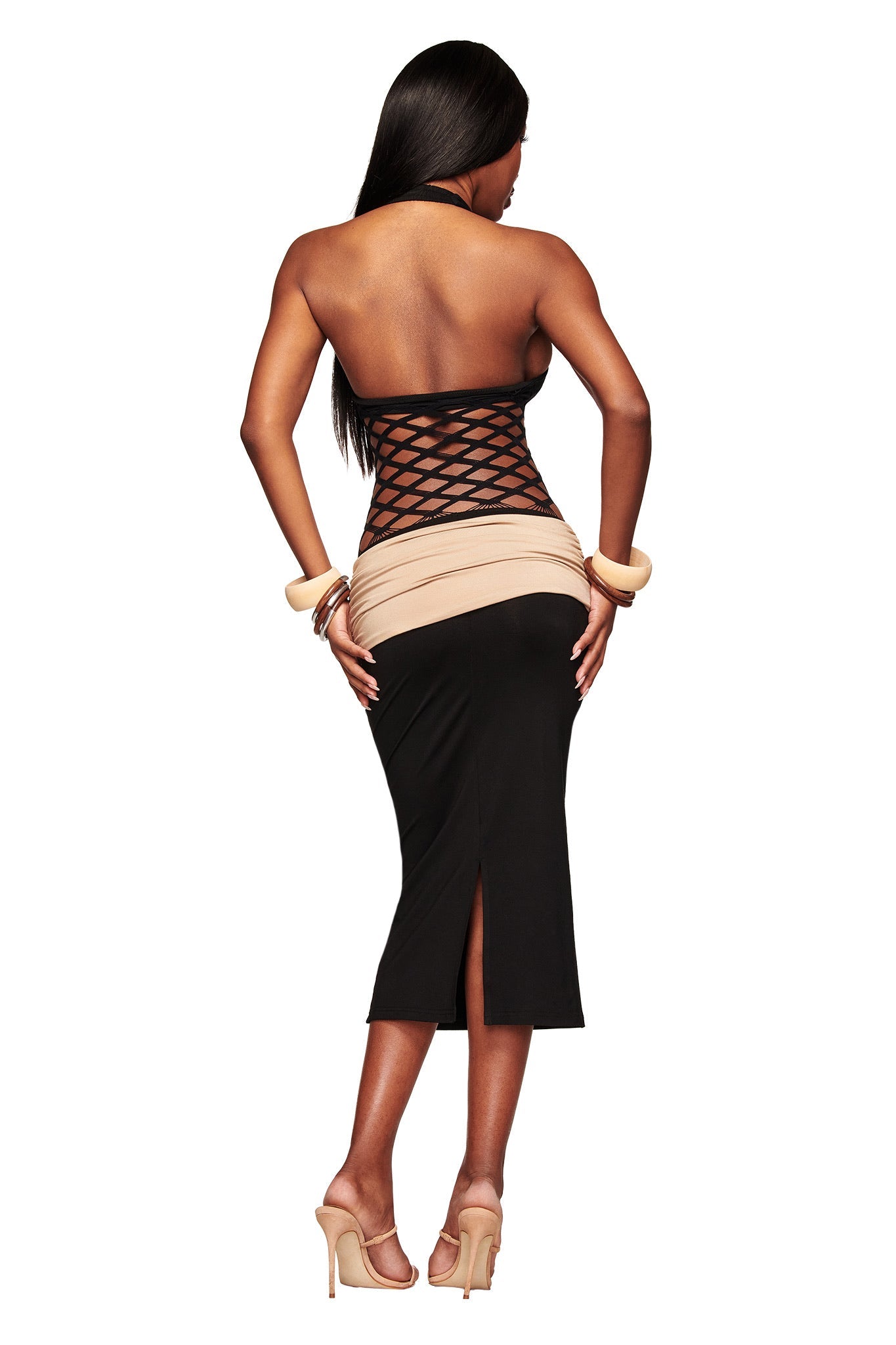 A woman with loose long hair wears the I.AM.GIA ZOREEN MIDI DRESS - BLACK, which features a black halter style, fishnet bodice panel, beige and black color blocks, and fitted skirt. She completes the look with high heels and bracelets.