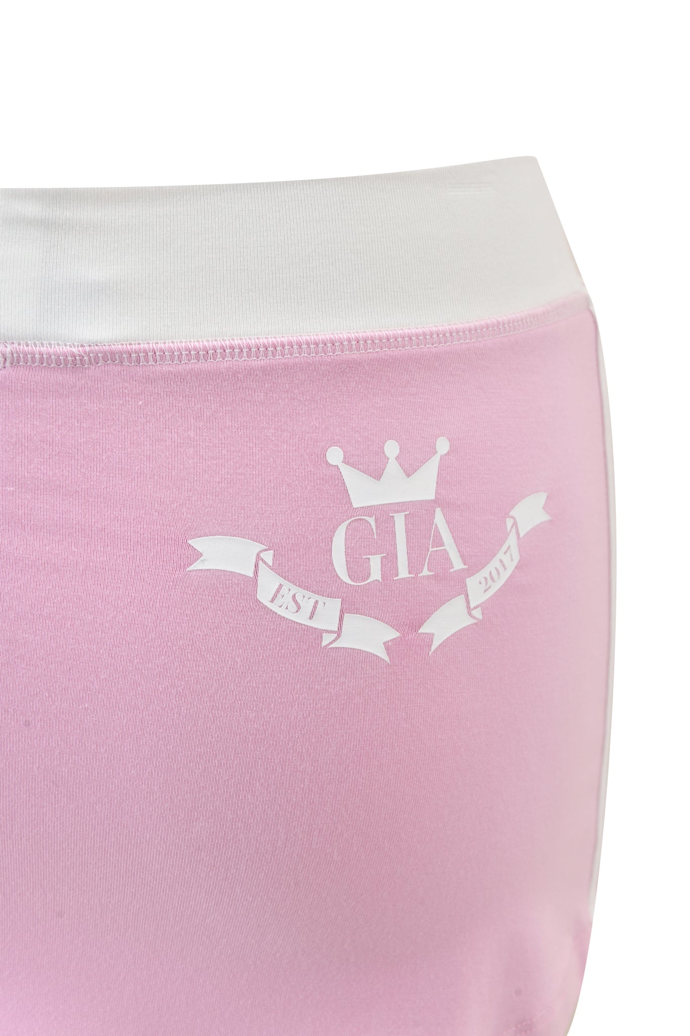 Close-up of buttery-soft BLARE PIPING TRACKPANT in baby pink viscose by I.AM.GIA, featuring a white waistband, crown graphic above "GIA," and ribbon with "EST. 2007." Perfect for sporty styles.