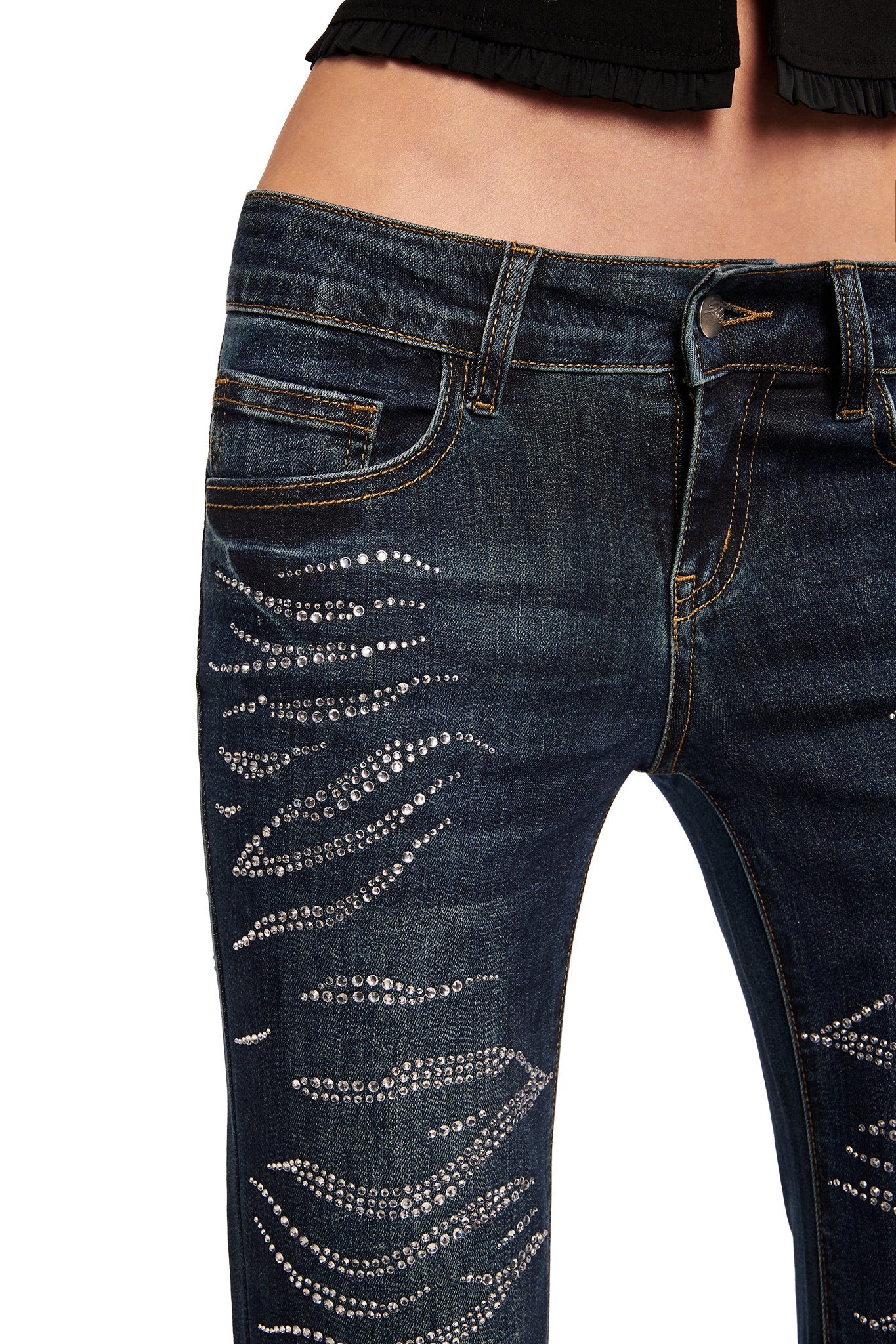 Close-up of a person wearing the I.AM.GIA JIJI DIAMONTE JEAN - BLUE, low-rise bootcut jeans with sparkling rhinestone patterns on the thighs, paired with a cropped black top.