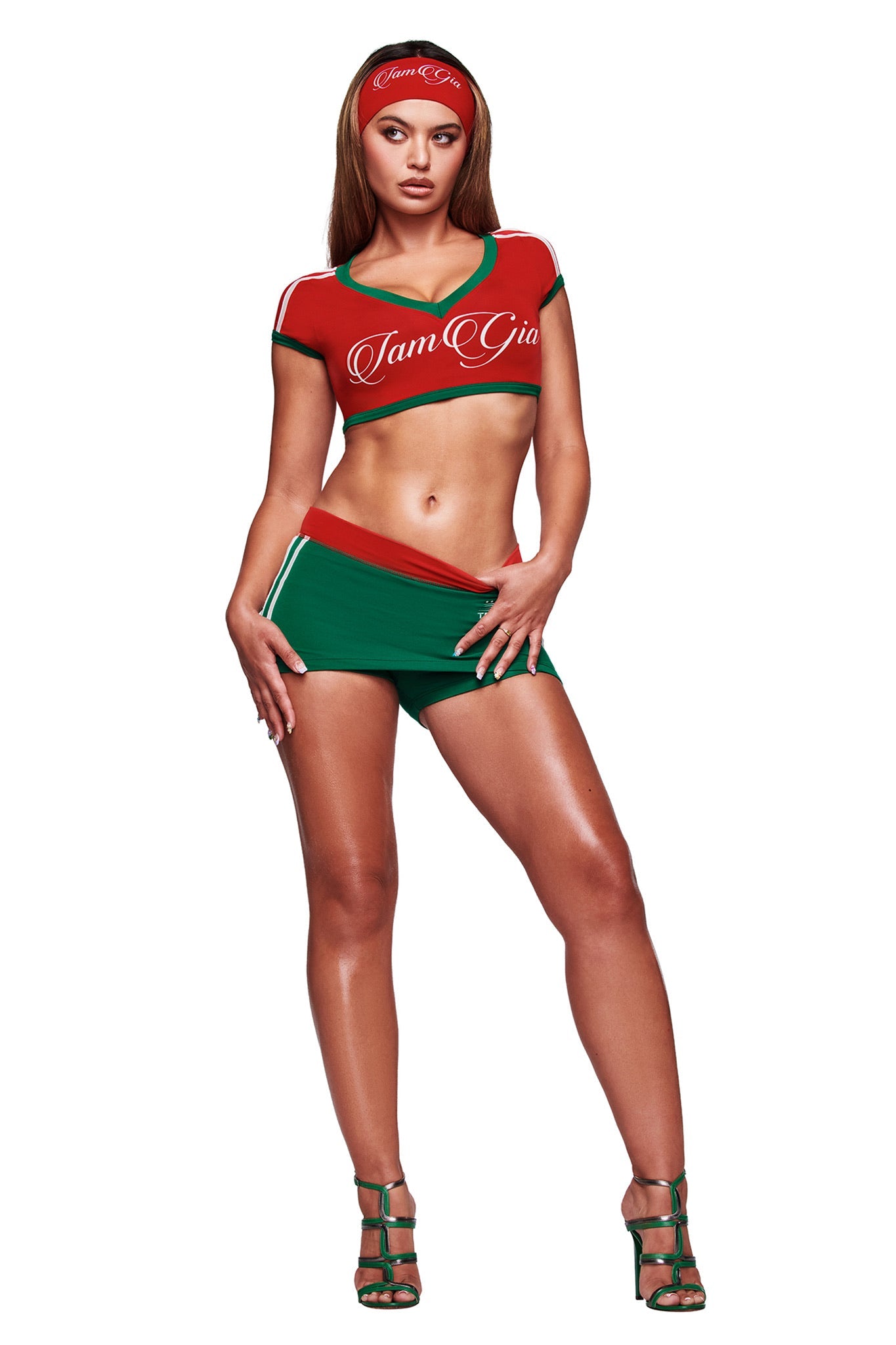 A woman poses in the I.AM.GIA BLARE TWO-PIECE SPORT CROP TEE in Crimson, paired with green striped shorts, green high-heeled sandals, and a red headband against a plain white background.