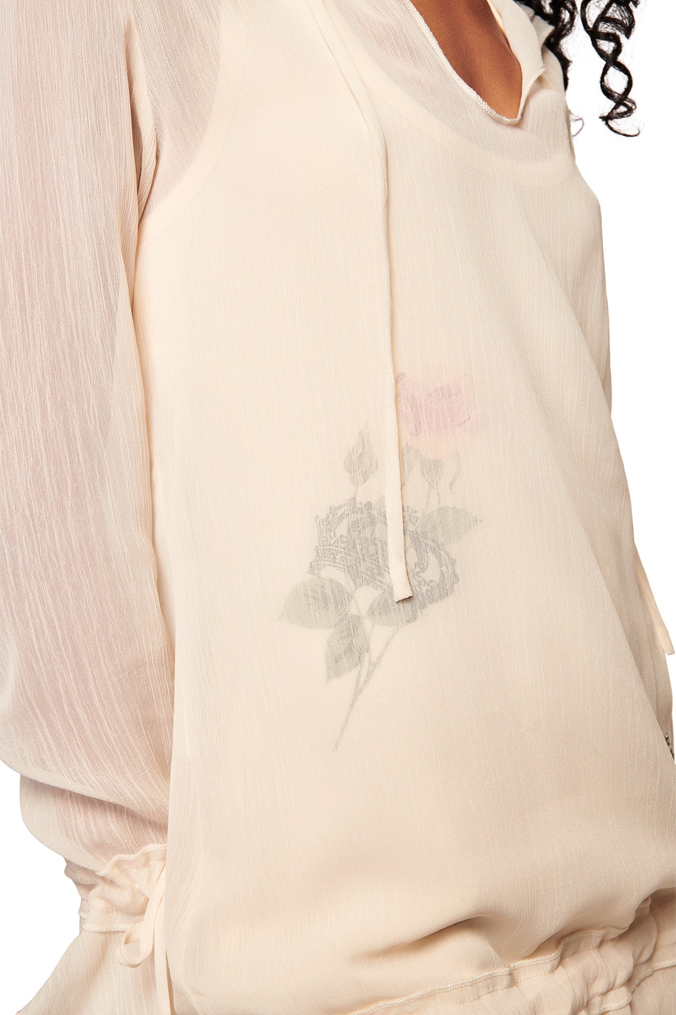 Close-up of the DIAMOND 2-IN-1 MINI DRESS in cream by I.AM.GIA, featuring sheer georgette with drawstring details and a subtle rose print. Part of the model’s neck and curly hair appear in the top right corner.