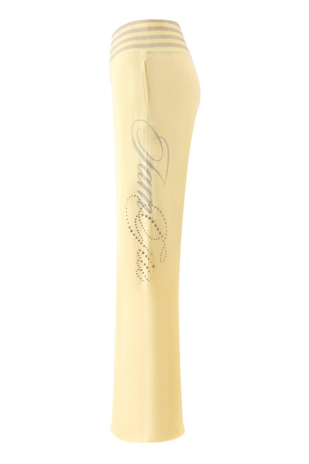 The VEDA PANT - YELLOW by I.AM.GIA are light yellow relaxed-fit track pants with a high waistband, three horizontal stripes, rhinestone embellishments, and script lettering along the side of the leg. Featuring a wide-leg silhouette, these pants are shown against a white background.