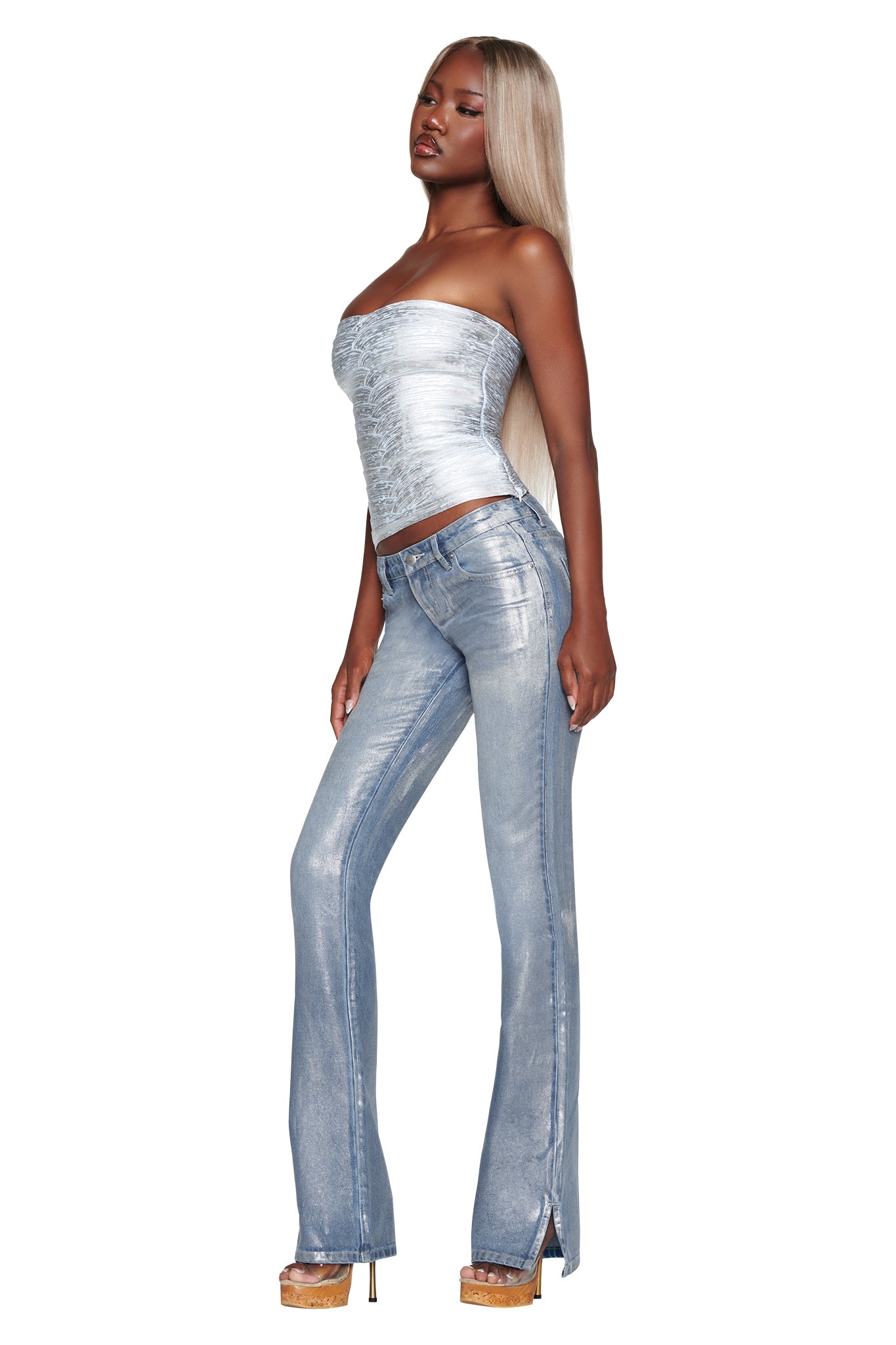 A woman with long blonde hair wears a silver strapless top, I.AM.GIA’s RENATA JEAN in Silver Metallic Wash featuring a mid-rise fit and straight leg silhouette, and beige platform heels while standing against a white background.