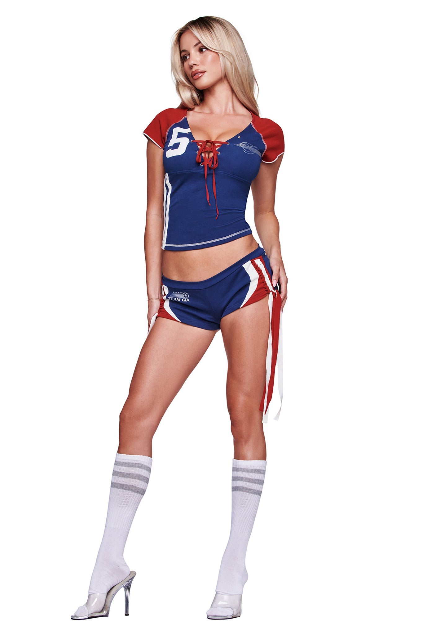 A woman wears the I.AM.GIA NOVIA LACE-UP T-SHIRT AND HEADBAND in navy, styled with short shorts, white knee-high socks, and high heels as she poses against a white background.