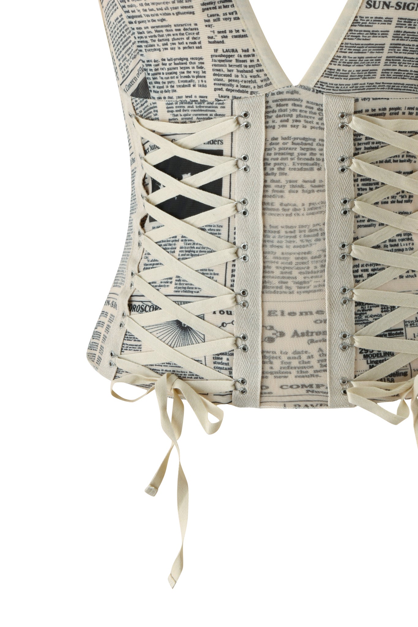 A close-up of the SORA TOP - LEFT ON READ by I.AM.GIA, a newspaper print corset top with cream laces, featuring eyelets and lace-up corset detailing with crisscrossed ribbon ties hanging at the hem.