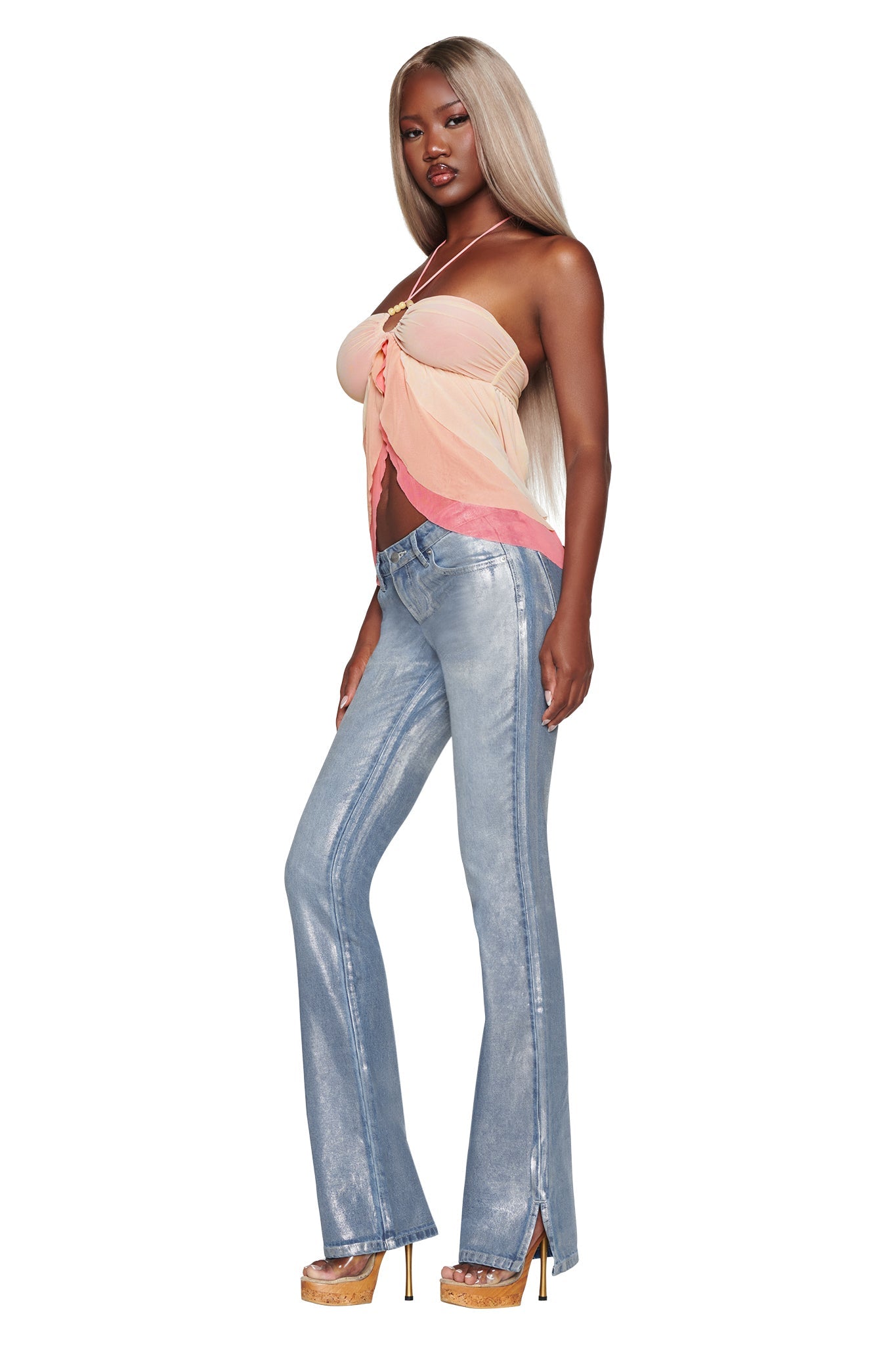 A woman with long blonde hair stands confidently against a white background, wearing the I.AM.GIA IDALIA TOP in Raspberry Multi—a strapless pastel top with cascading ruffles—paired with light blue flared jeans and tan platform heels.