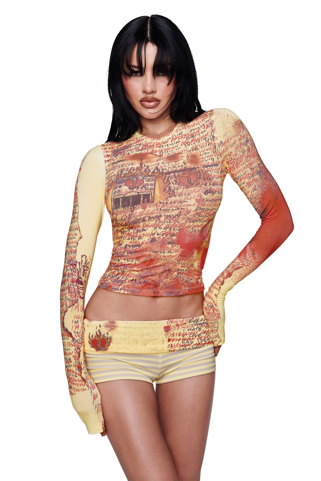 A woman with long dark hair wears the I.AM.GIA T-REX BLARE 2.0 LONG SLEEVE TEE in yellow, styled with matching shorts featuring handwritten script and vintage illustrations in yellow and orange tones, standing against a plain white background.