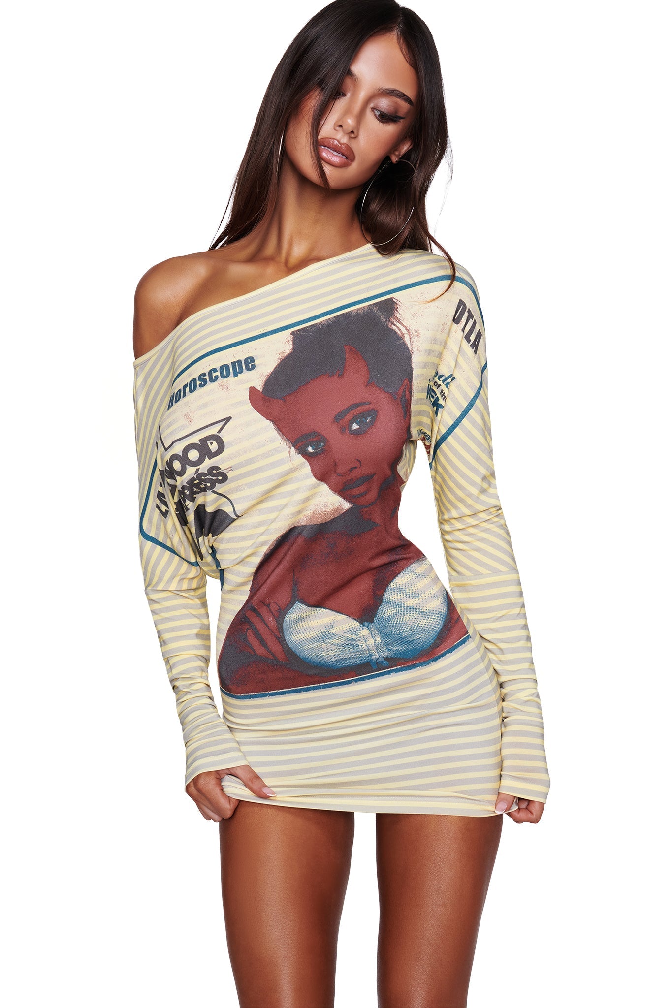 A woman wears the I.AM.GIA T-REX GISELLE OFF SHOULDER MINI DRESS in yellow, an off-shoulder batwing dress featuring bold stripes and a graphic cartoon devil girl with the words “Horoscope” and “Blood Drips,” standing against a white background.